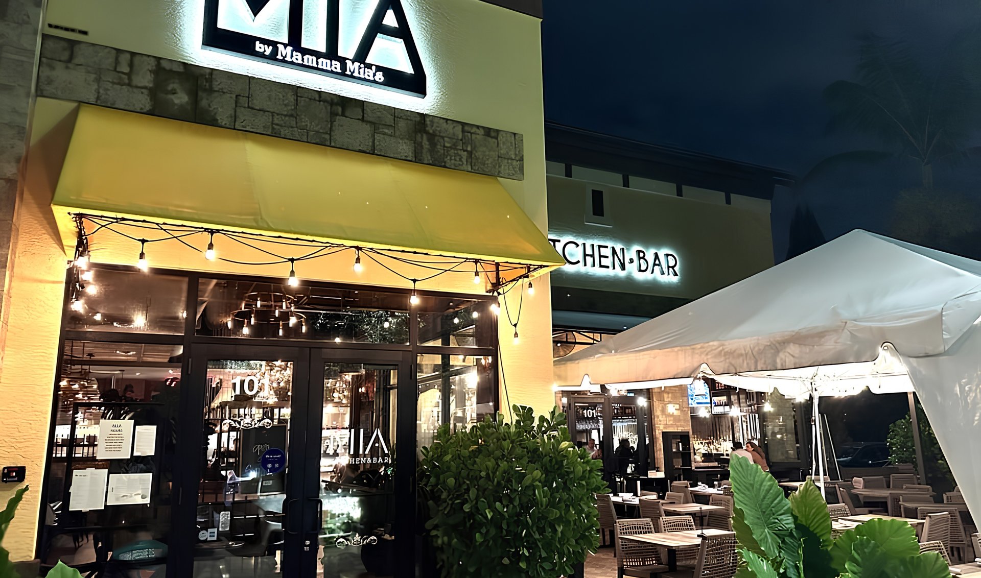 MIA by Mamma Mia's restaurant exterior at night, with a yellow awning and tented patio seating.