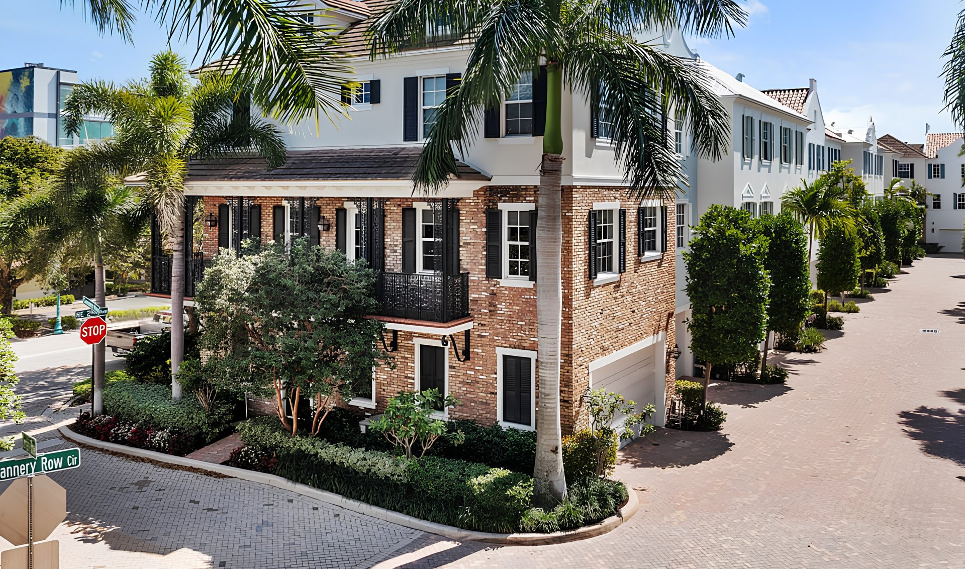 Boutique condo building with a brick facade, white upper stories, and palm trees along a paved courtyard.