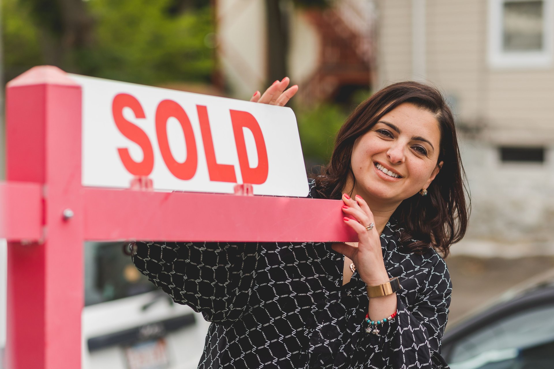 a realtor smiling and holding a sold sign post outside a house