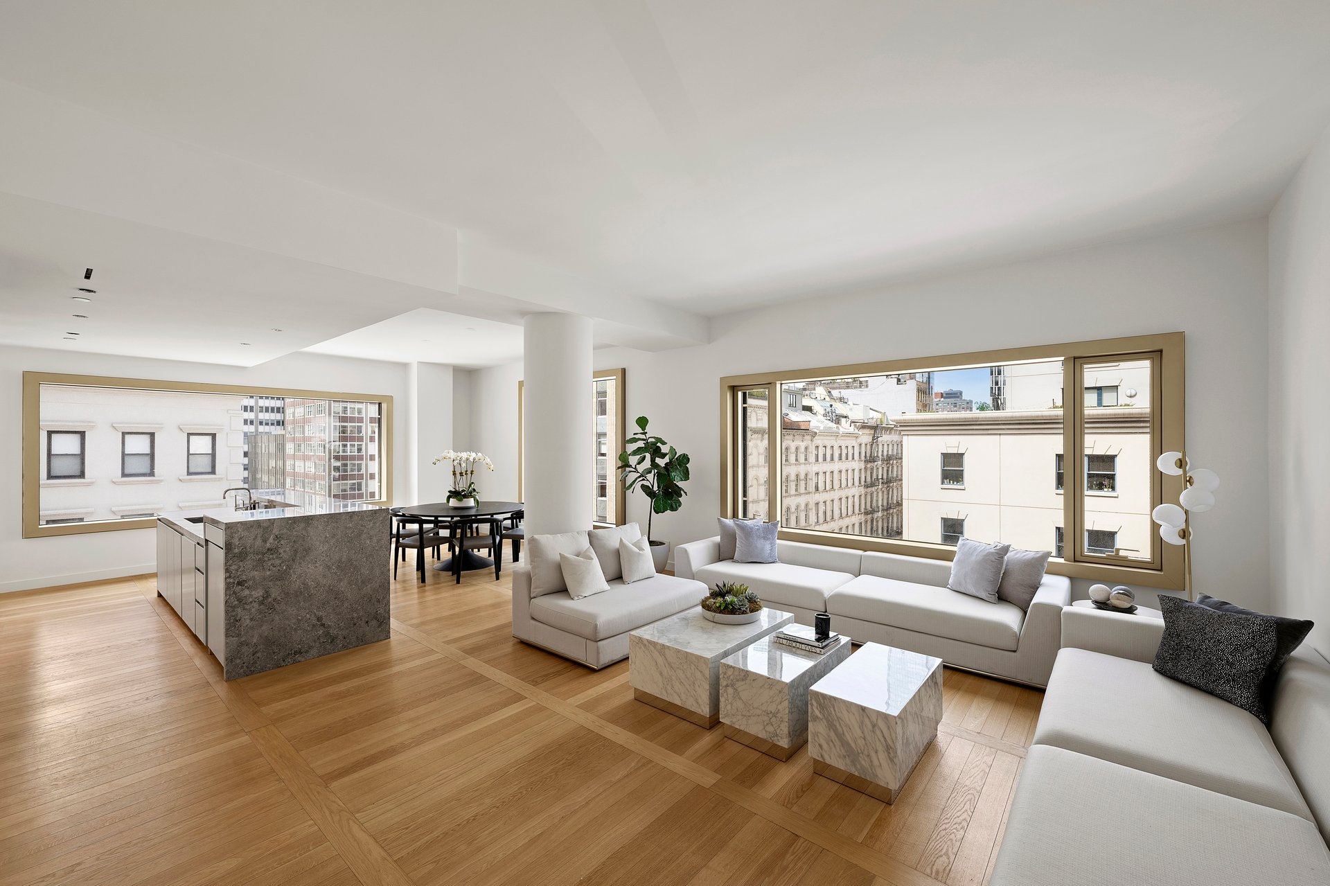 Open-plan living room with a white sectional, marble coffee tables, and large city-view windows.
