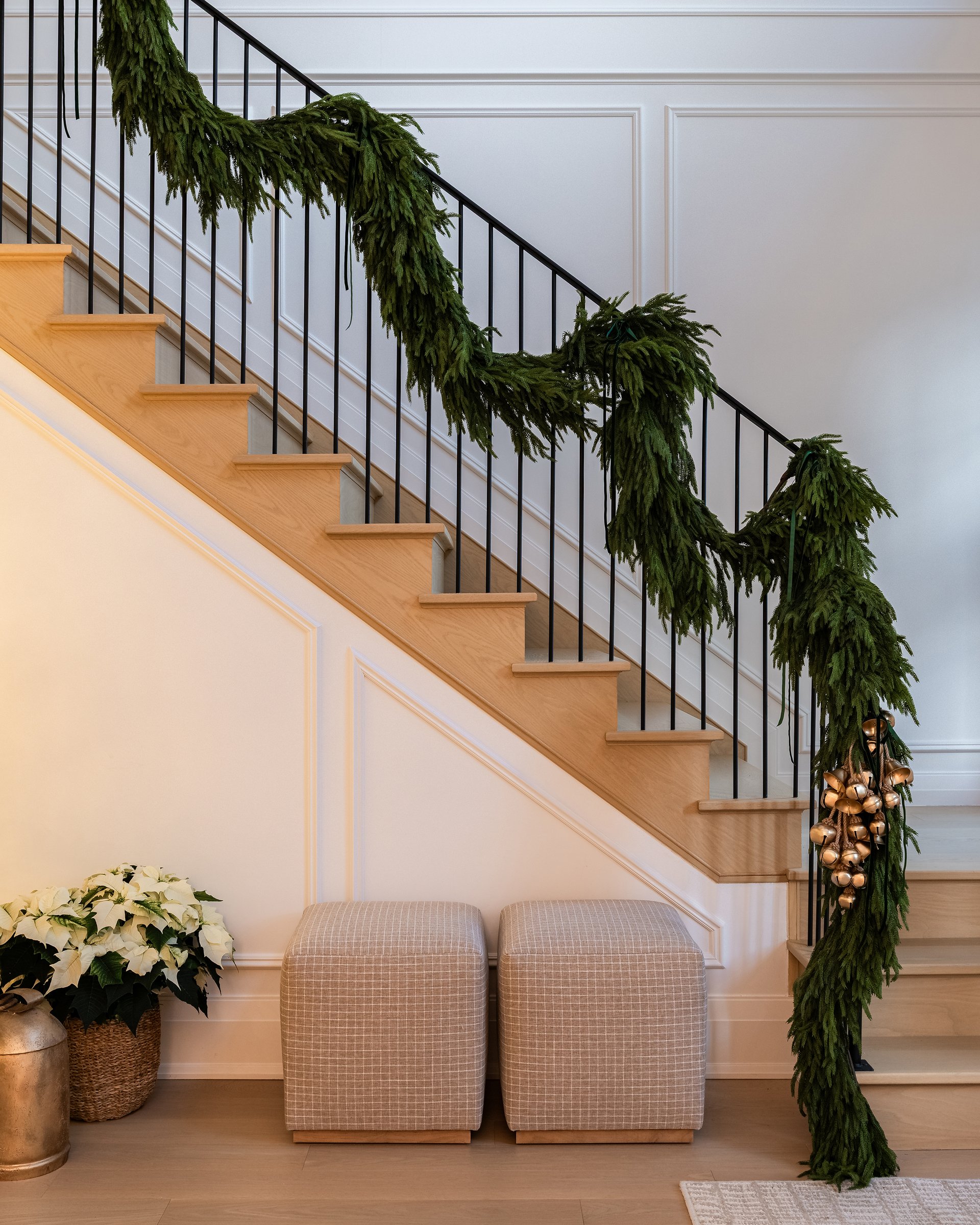 Staircase in an Oakville custom home decorated with lush greenery garland and gold holiday bells.