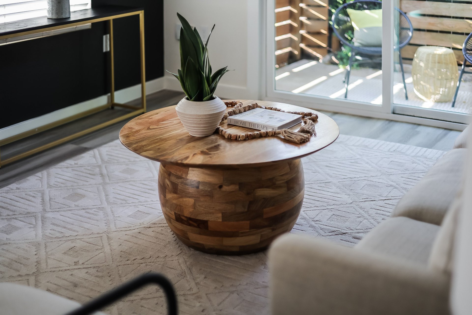 Living room with a round wood coffee table, potted plant, geometric rug, and sliding glass doors to a patio.