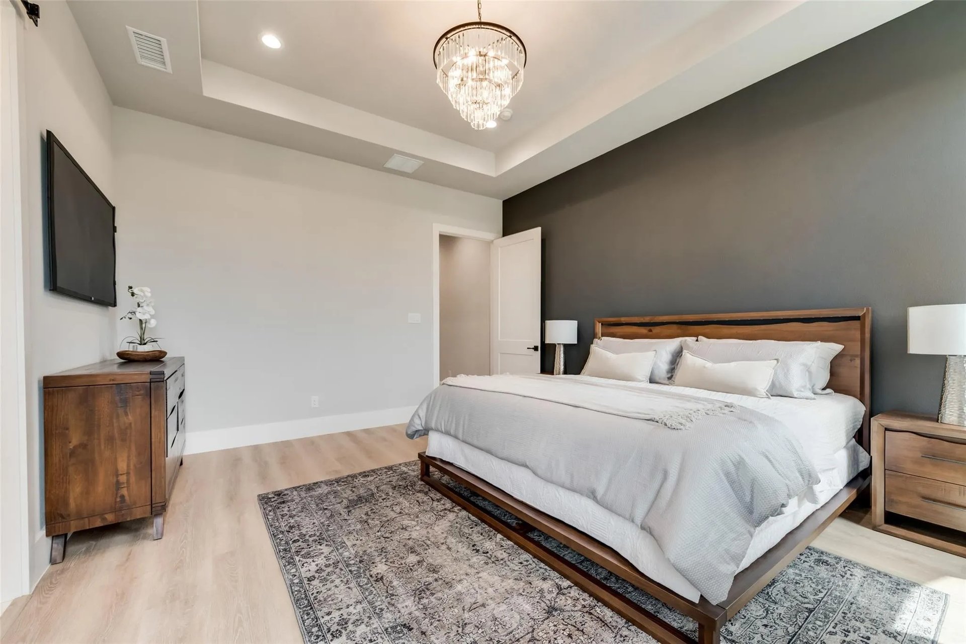 Staged bedroom with a wood-frame bed, dark accent wall, and crystal chandelier.