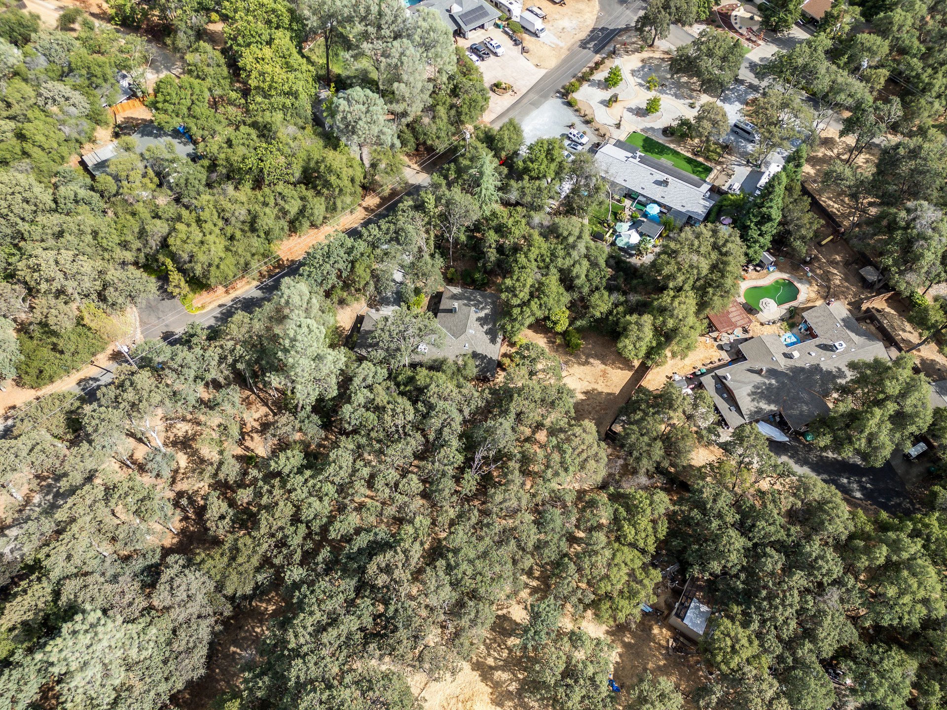 Aerial view of a wooded residential property, with a partly visible house and neighboring homes nearby.