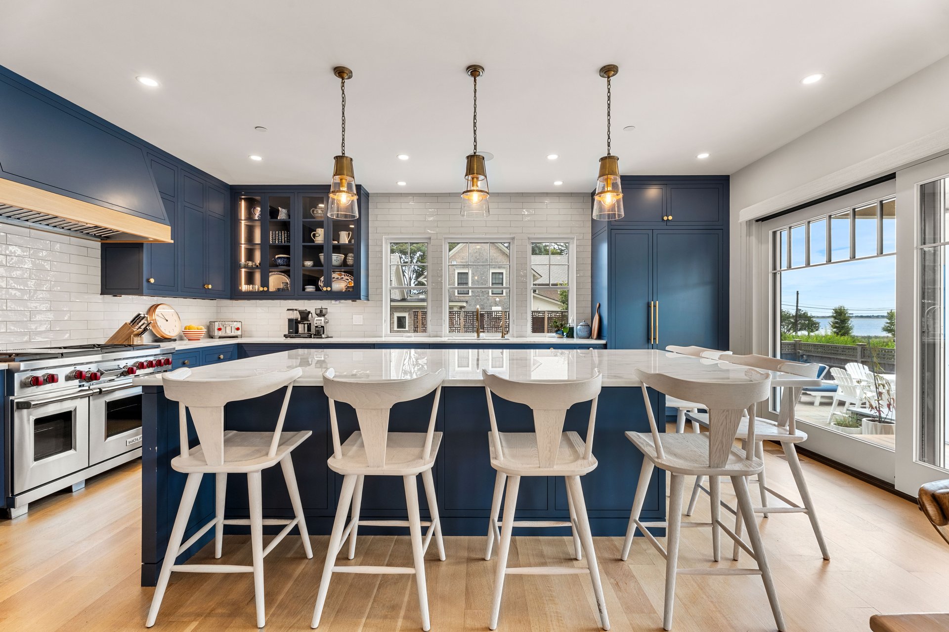 Kitchen with navy cabinetry, a white island and stools, and windows overlooking the water.