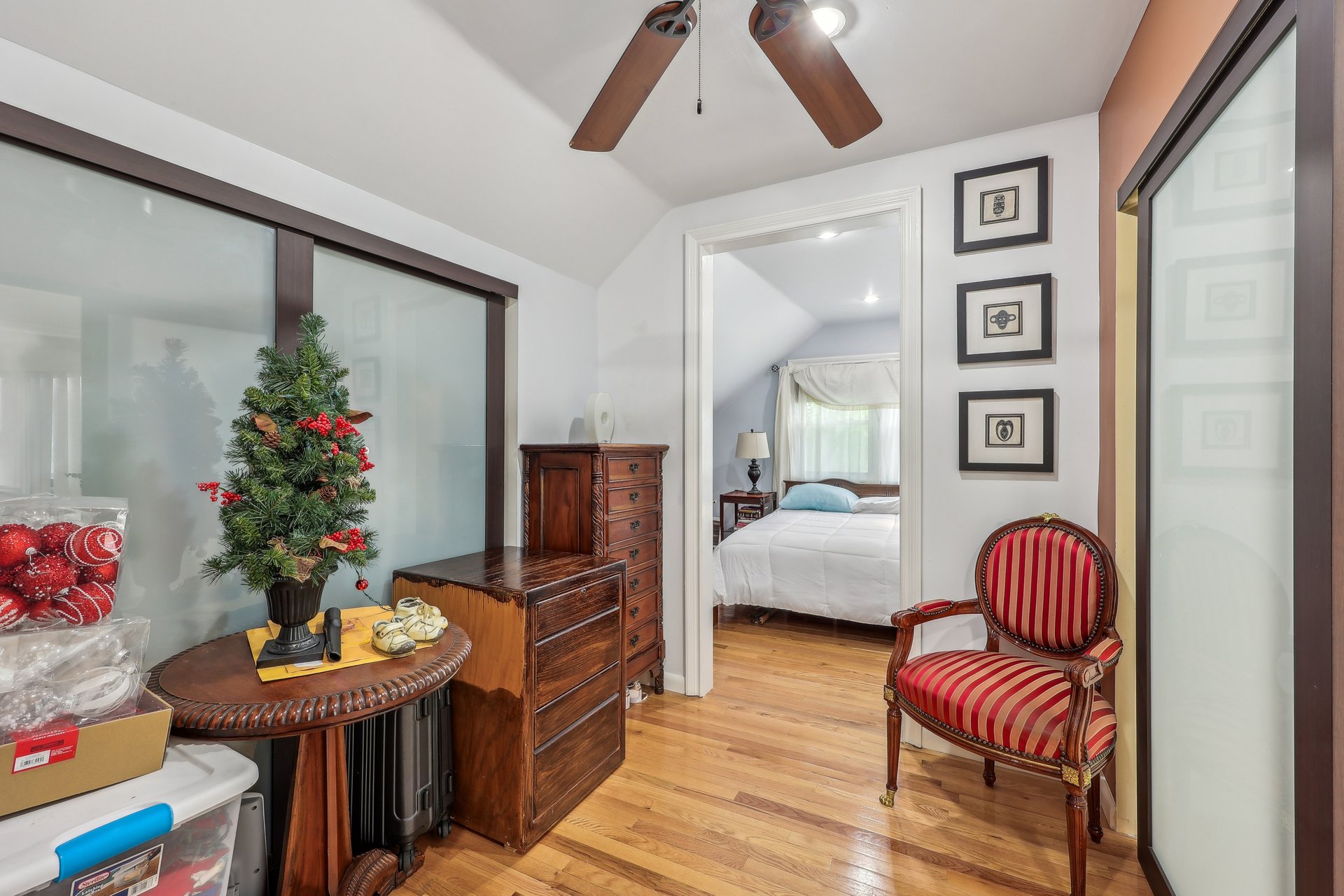 Furnished hallway with frosted glass doors, a red striped armchair, and a view into a bedroom.