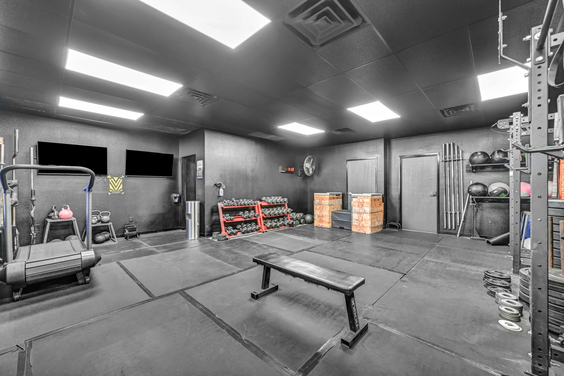 Gym with dumbbell racks, a weight bench, treadmill, and squat rack on rubber flooring.