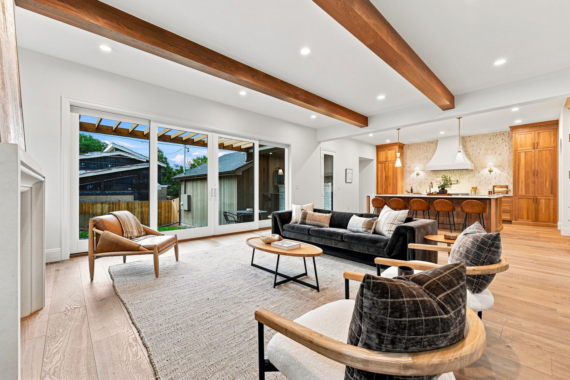 Open-plan living room with exposed wood beams, sliding glass doors, and a dark sofa beside the kitchen.