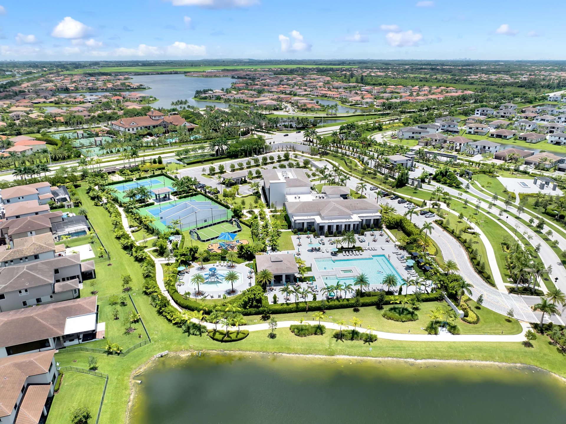 Aerial view of a lakeside community with a clubhouse, pool, and tennis courts.