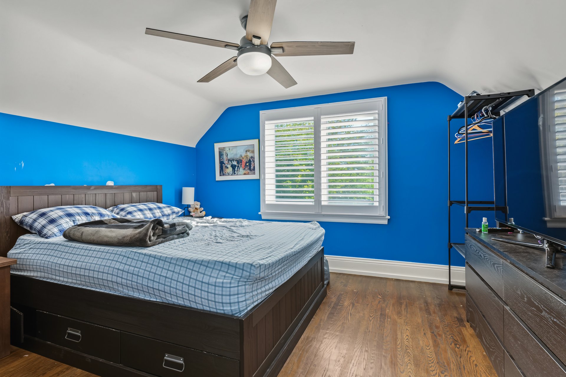 Bedroom with bright blue walls, a dark wood bed, shuttered windows, and wood flooring.