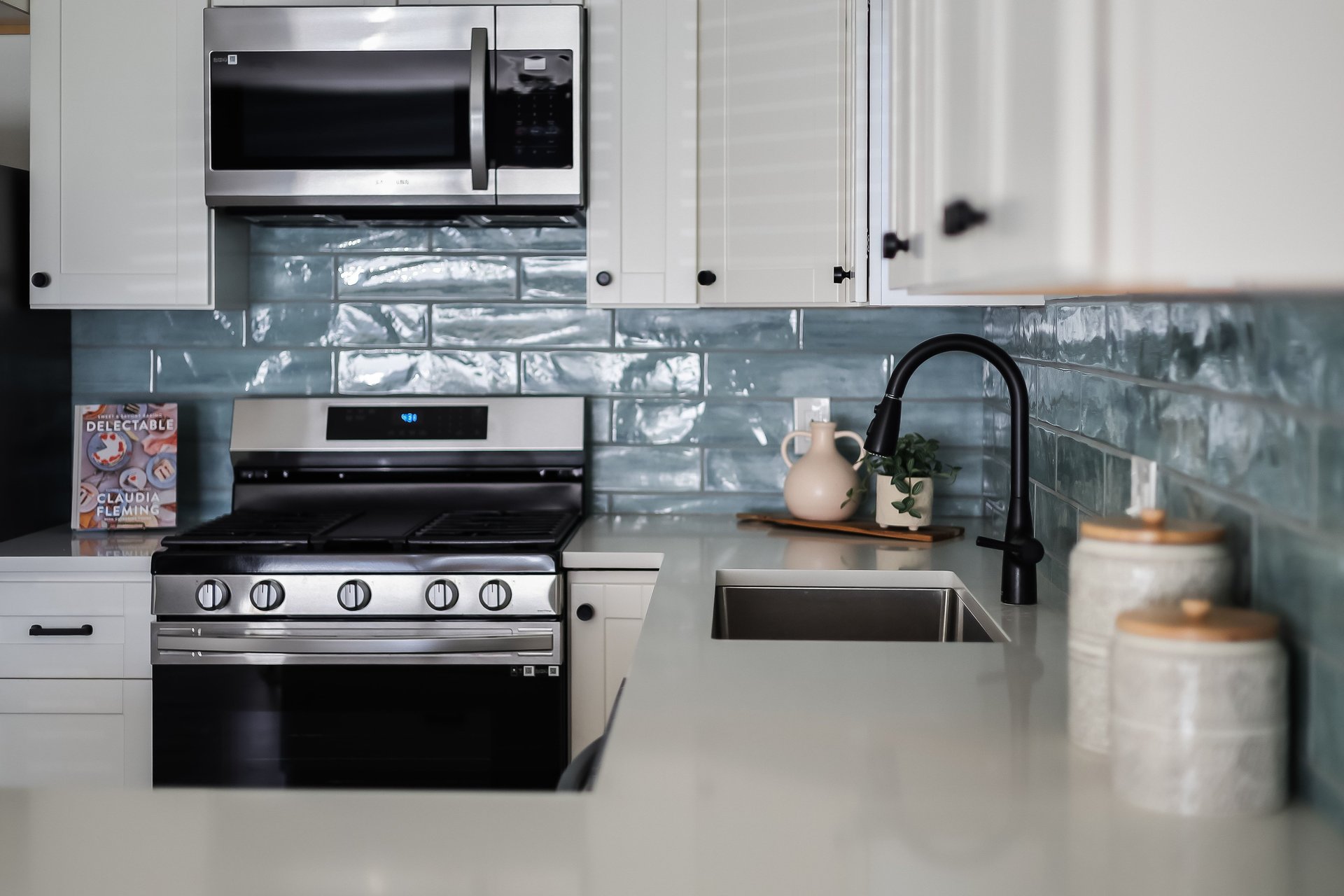 Kitchen with white cabinets, blue-gray tile backsplash, stainless-steel appliances, and a deep sink.