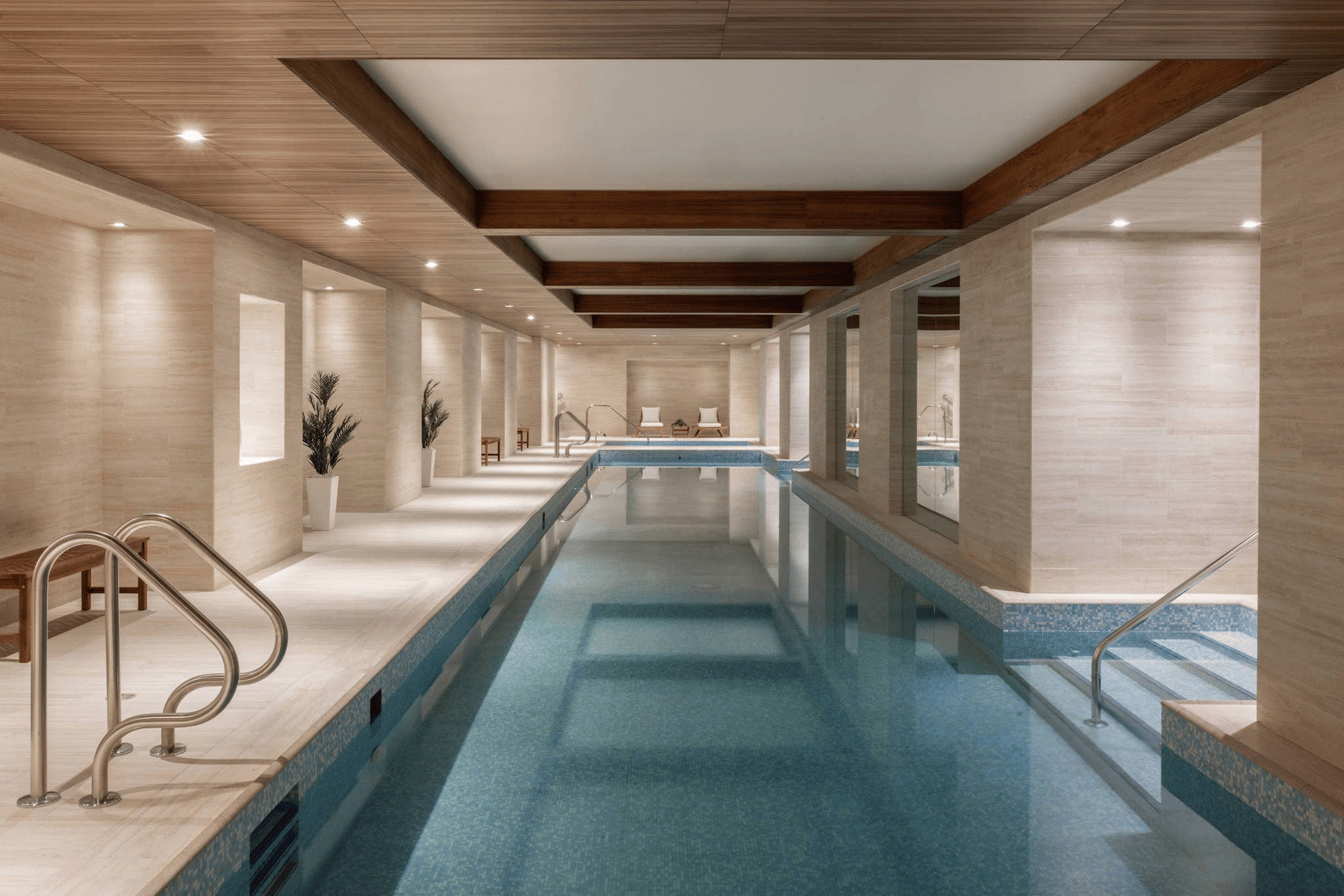Indoor swimming pool with stone finishes, wood ceiling beams, and stainless-steel handrails.