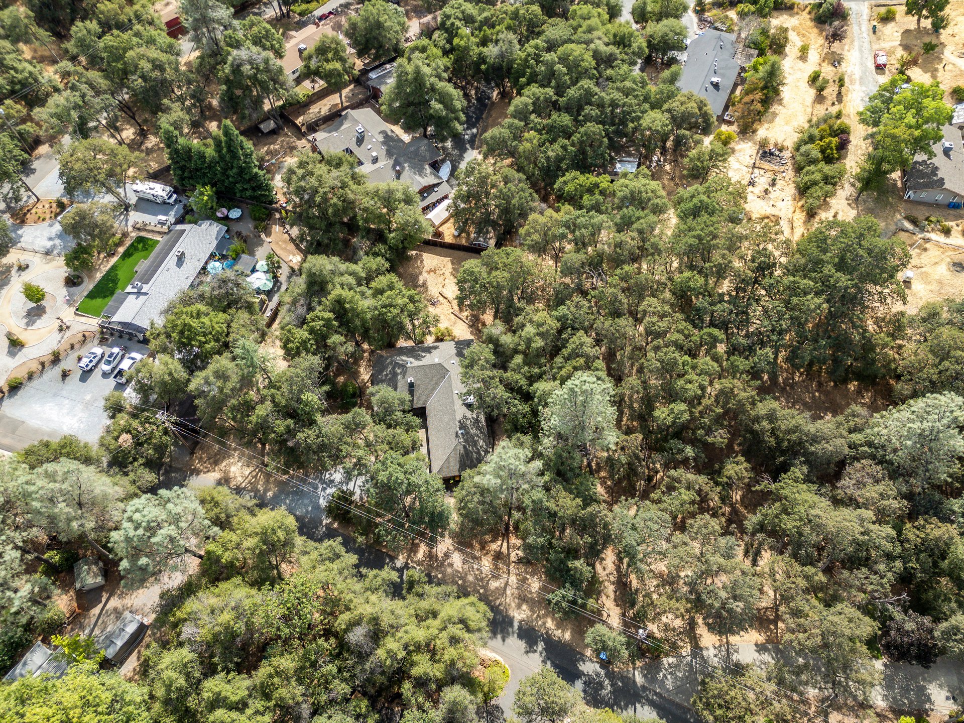 Aerial view of homes among dense trees, with a dry cleared area beside the neighborhood.