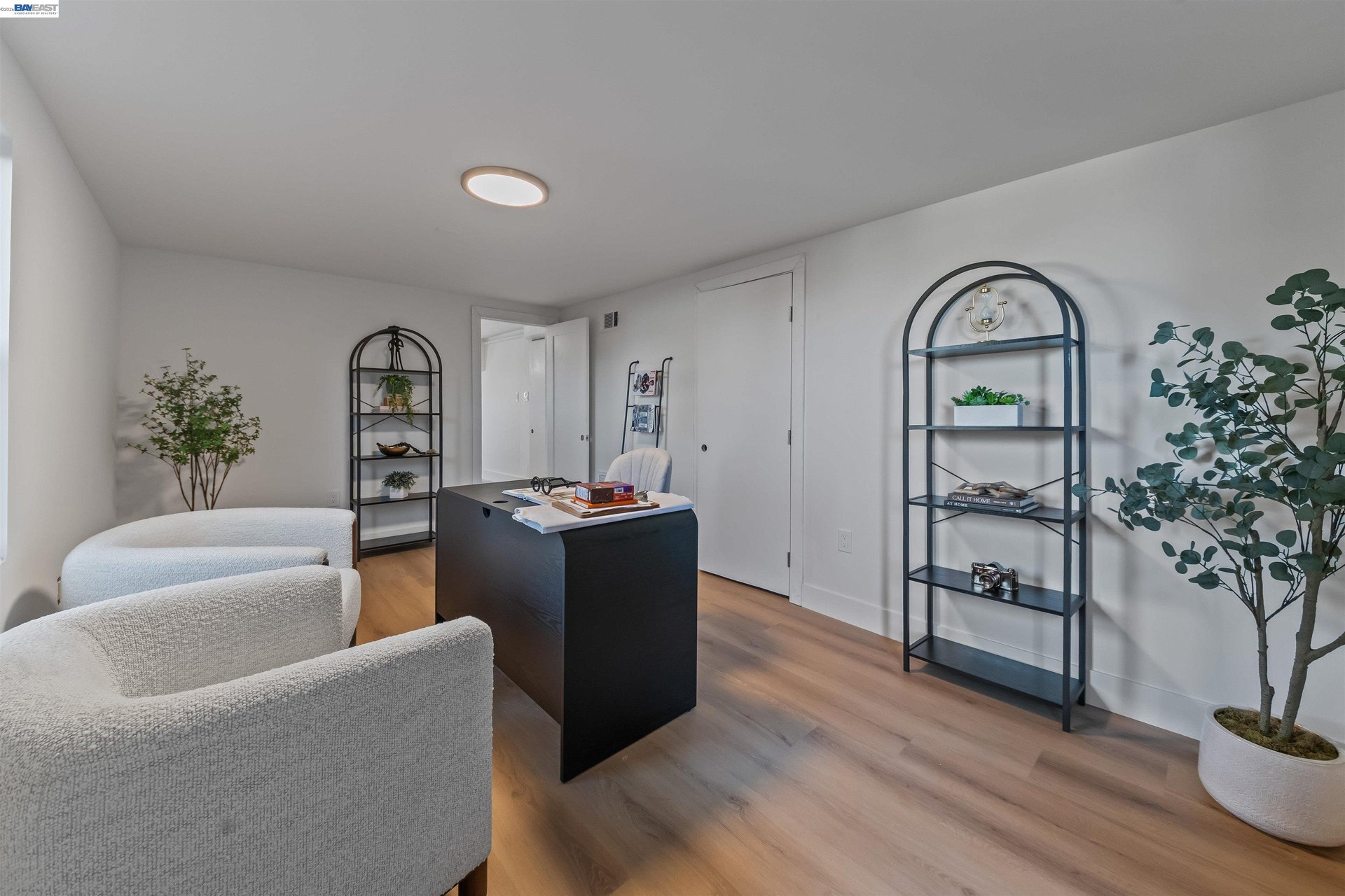 Furnished home office with a black desk, white chairs, and arched shelving.