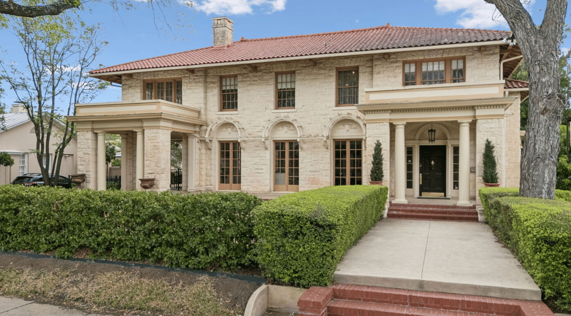 Two-story stone home with a red tile roof, arched windows, and a columned entrance.
