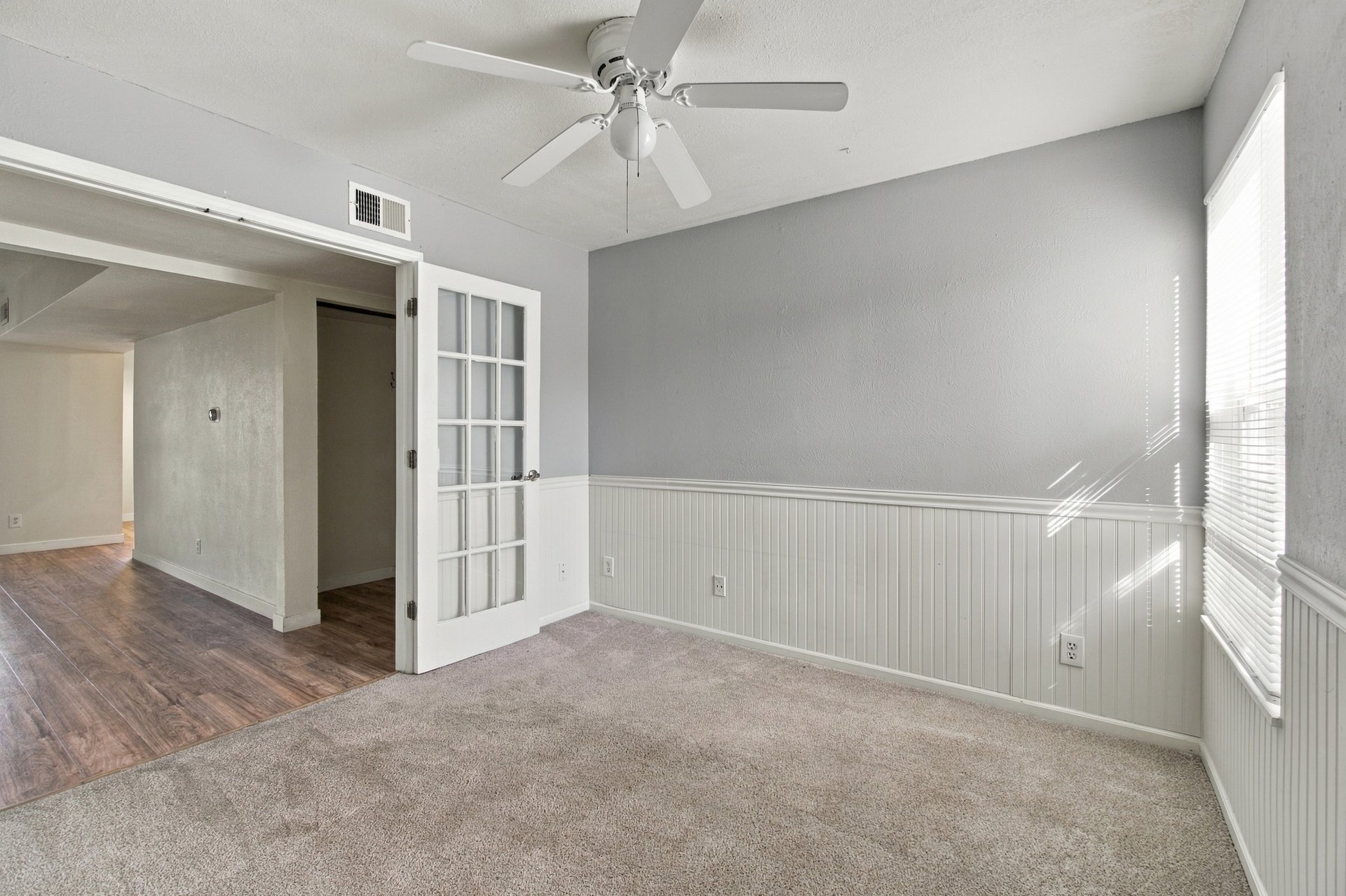 Empty carpeted room with gray walls, white beadboard wainscoting, and a ceiling fan.