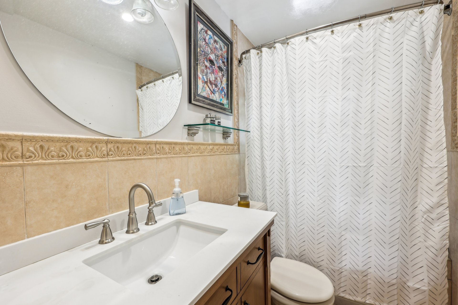 Bathroom with a white vanity, beige tile, patterned shower curtain, and toilet.