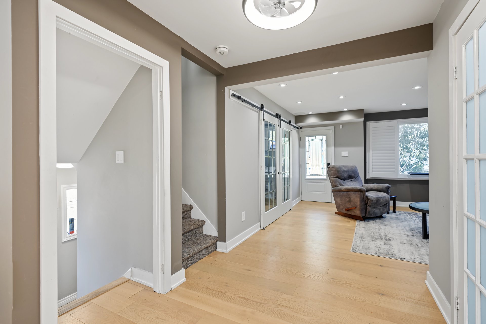 Living area with light hardwood floors, glass sliding doors, carpeted stairs, and a gray recliner.