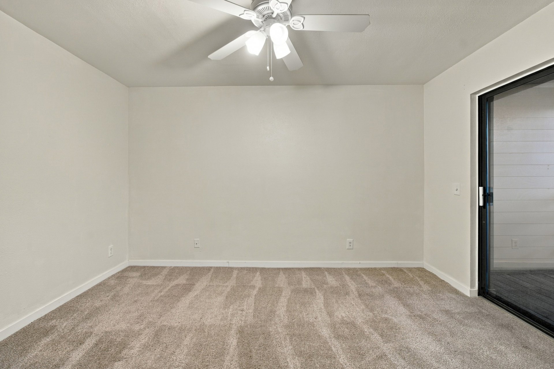 Empty carpeted bedroom with a ceiling fan and sliding glass door to a balcony.