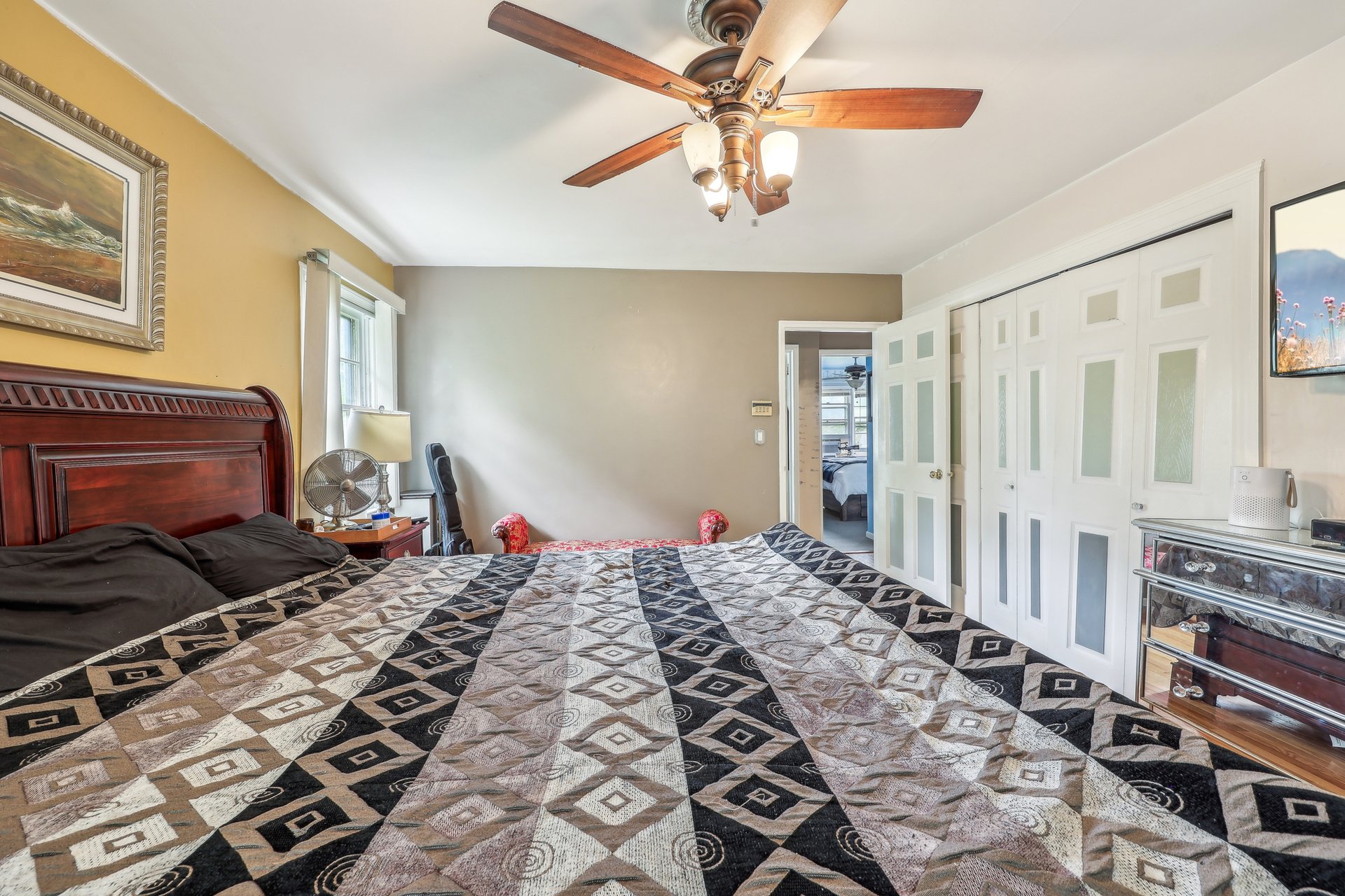 Bedroom with a geometric quilt, wood ceiling fan, white closet doors, and an open doorway.