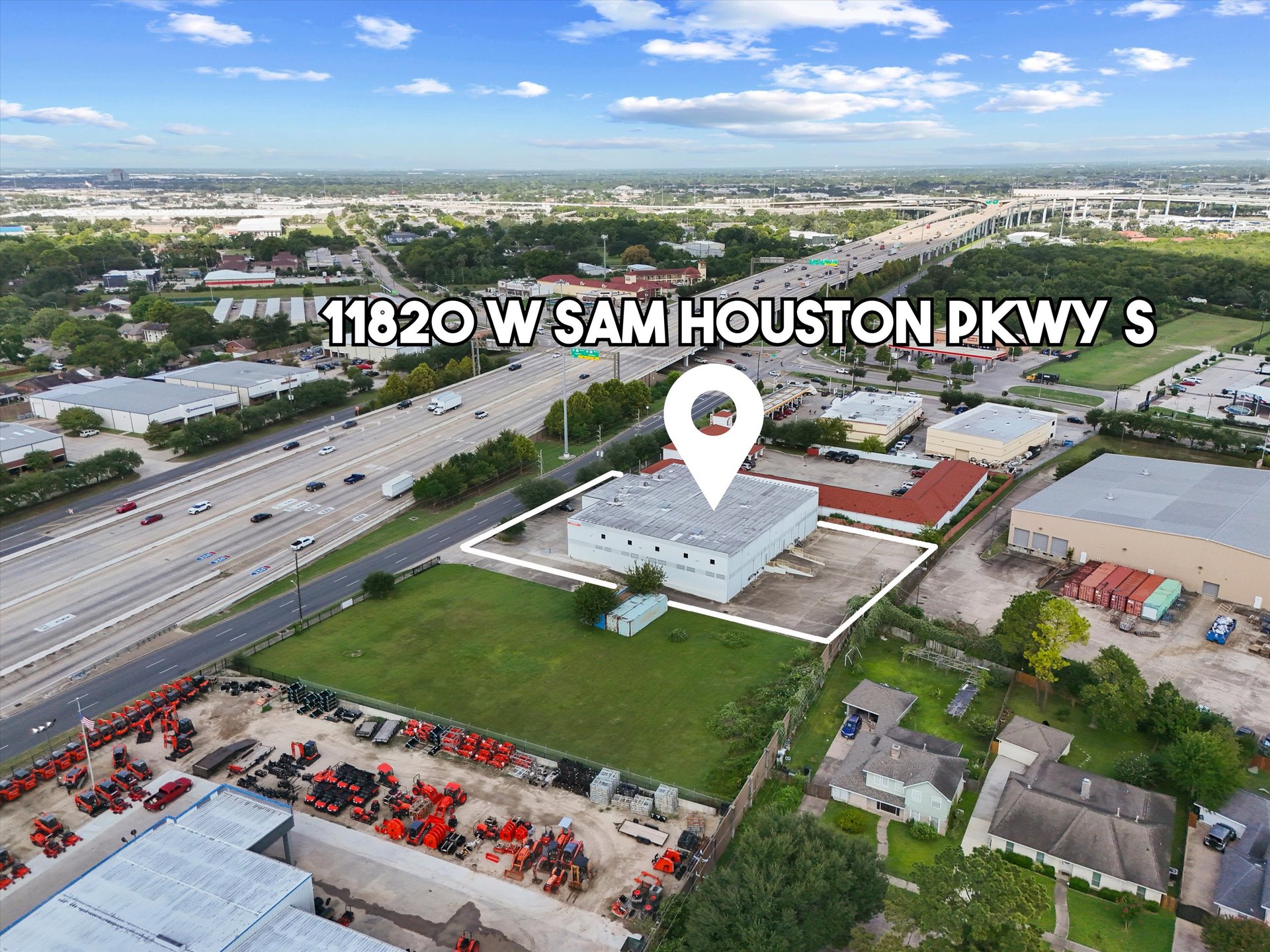Aerial view of a warehouse lot outlined beside a busy highway, with a map pin marking the building.