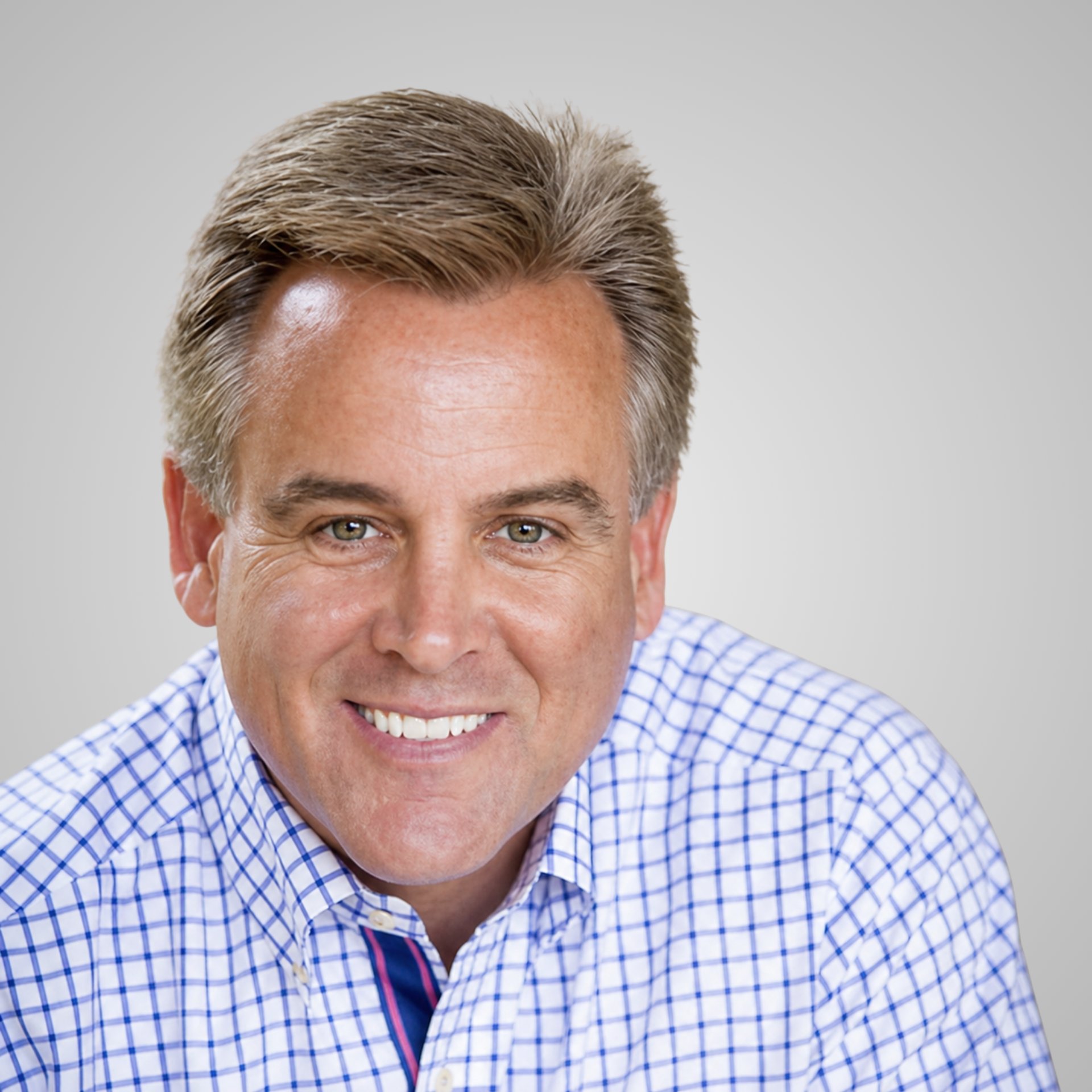 Rich Fahey smiling in a blue-and-white checkered shirt and striped tie.