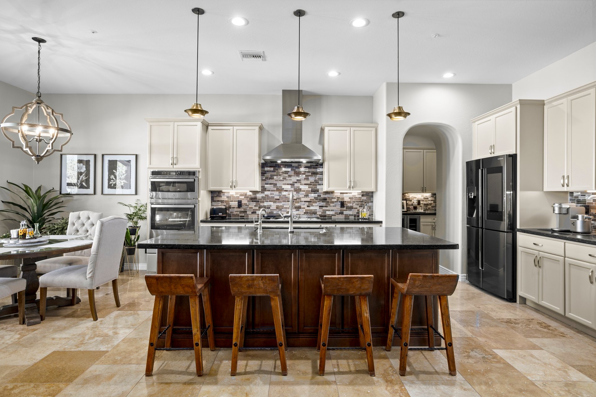 Spacious modern kitchen with a large dark island, pendant lights, white cabinets, black appliances, and a small dining nook.