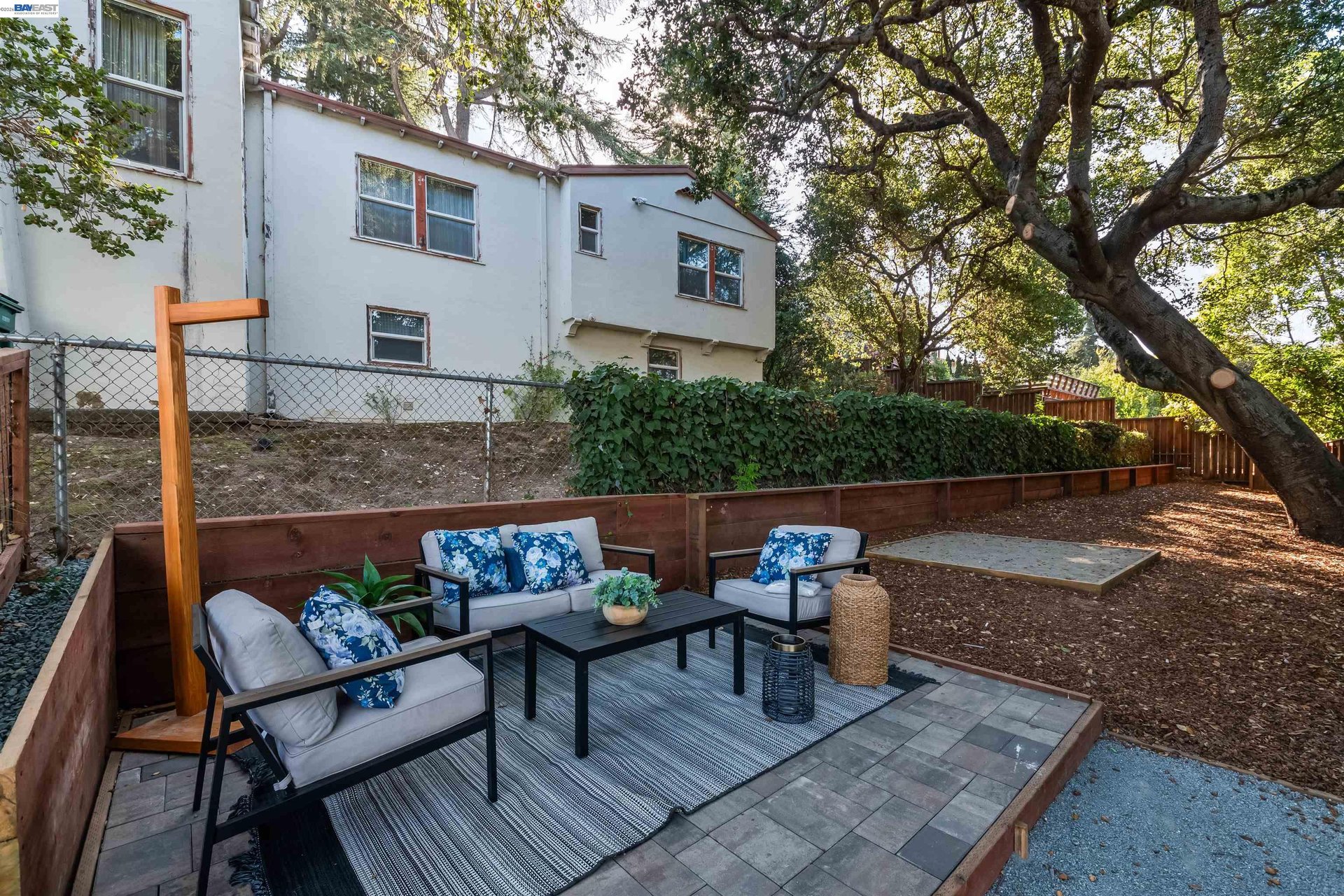 Backyard patio with cushioned seating, raised planters, and a large shade tree.