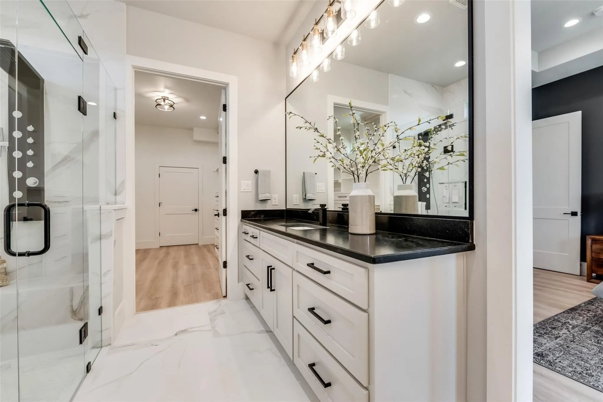 Renovated bathroom with a white vanity, black countertop, large mirror, and glass-enclosed shower.