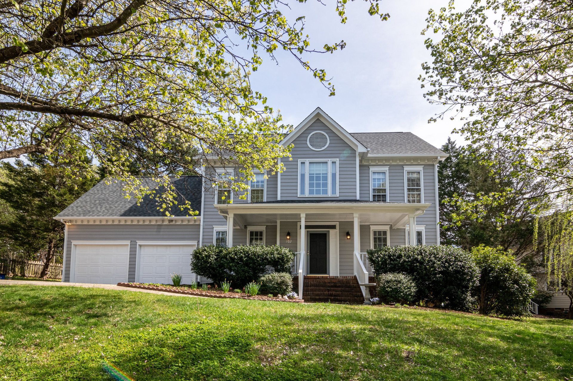 a white two story single family house surrounded by plants and trees