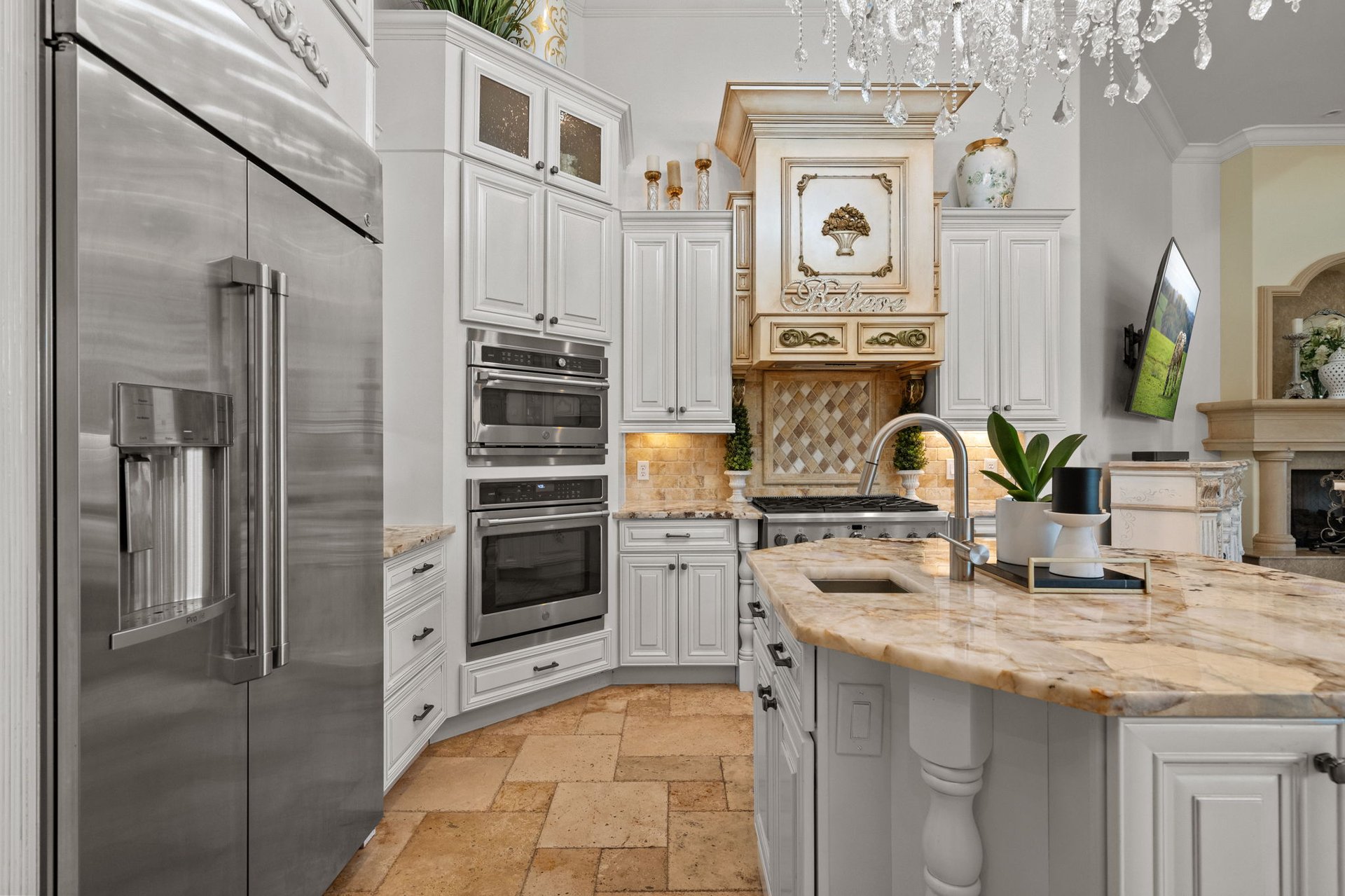 Ornate white kitchen with stainless steel appliances, a marble island, and a decorative range hood.
