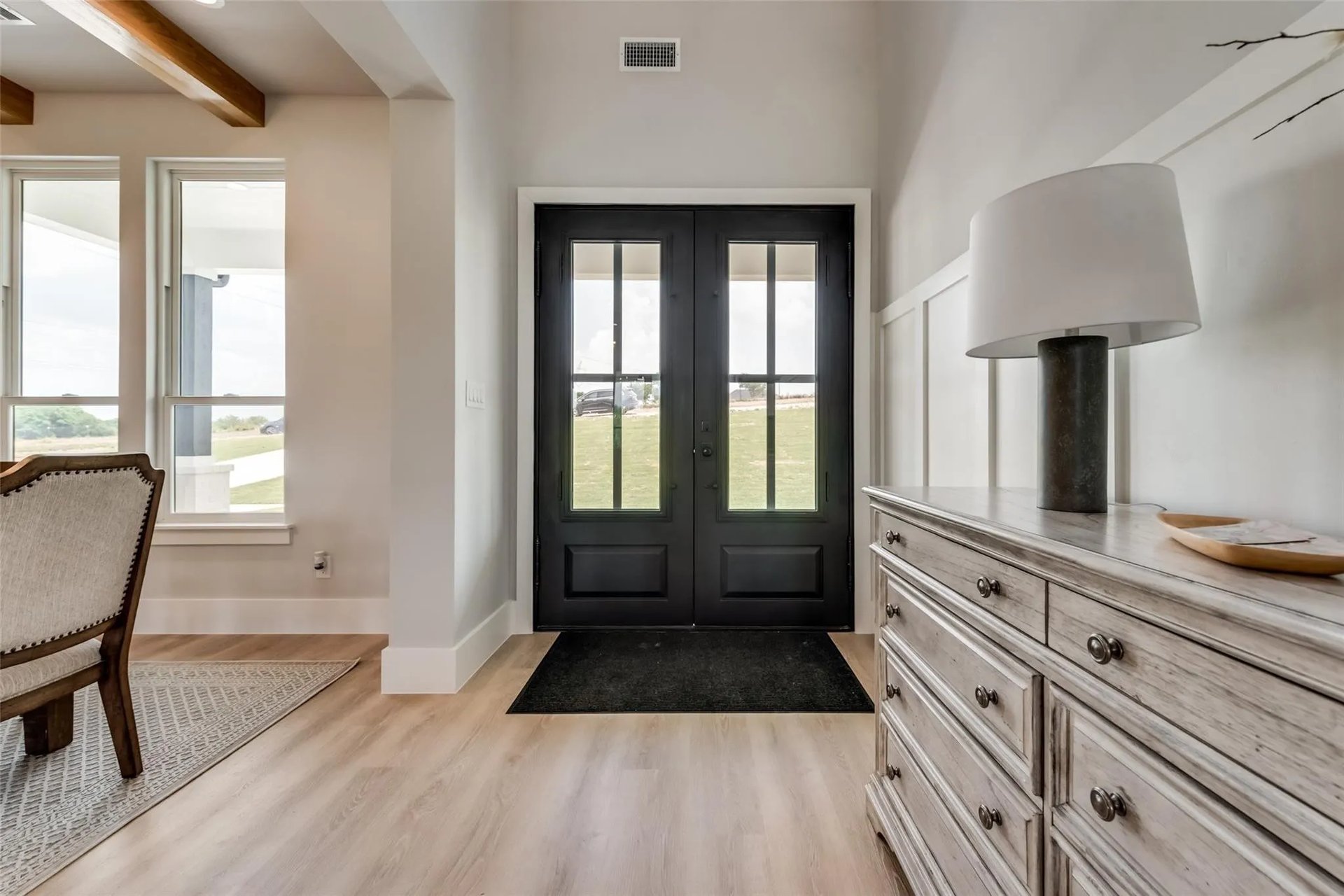 Foyer with black glass-paneled double doors, tall windows, and a distressed wood dresser.