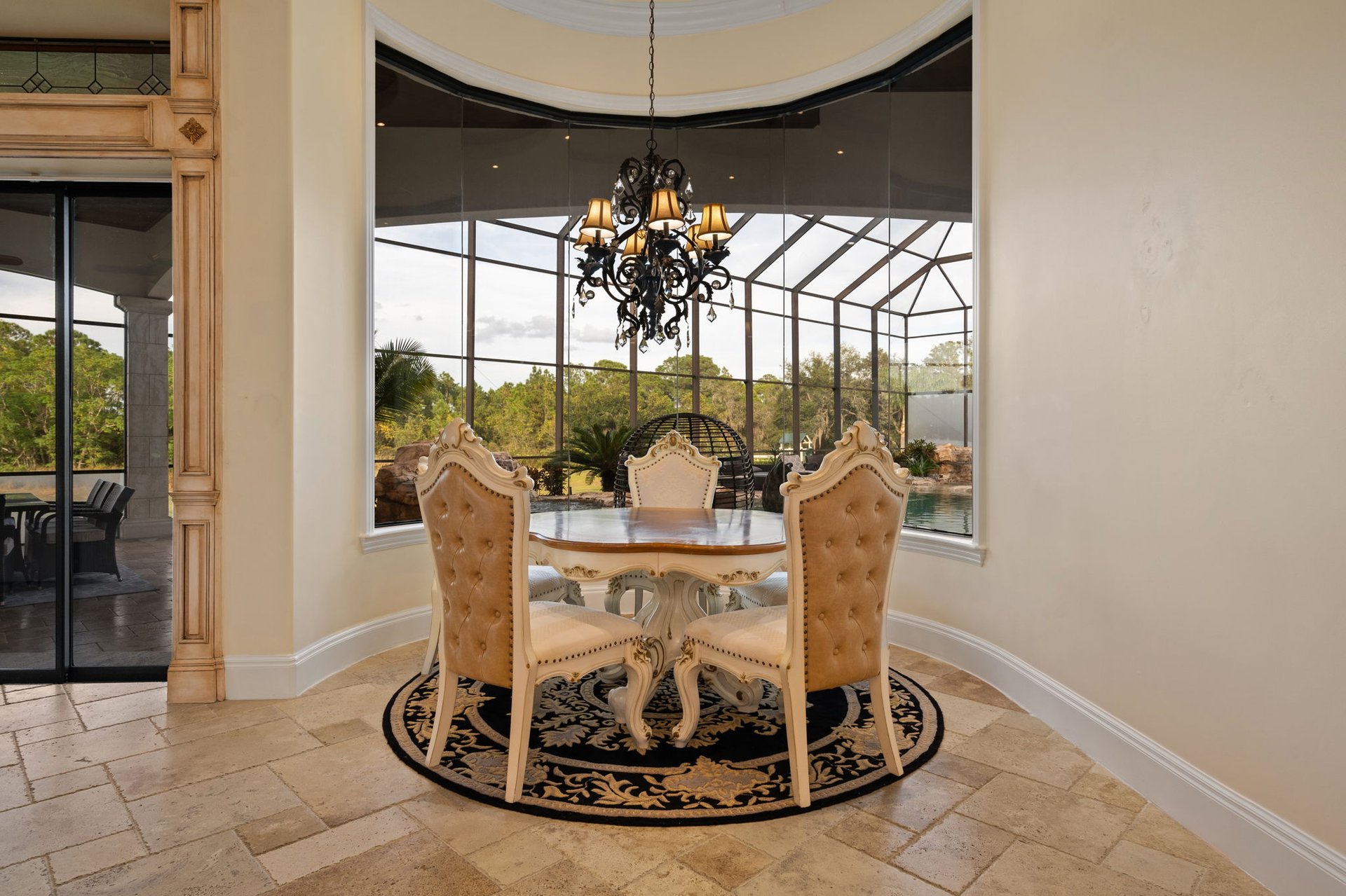 Dining area with an ornate table and chandelier overlooking a glass-enclosed patio and pool.