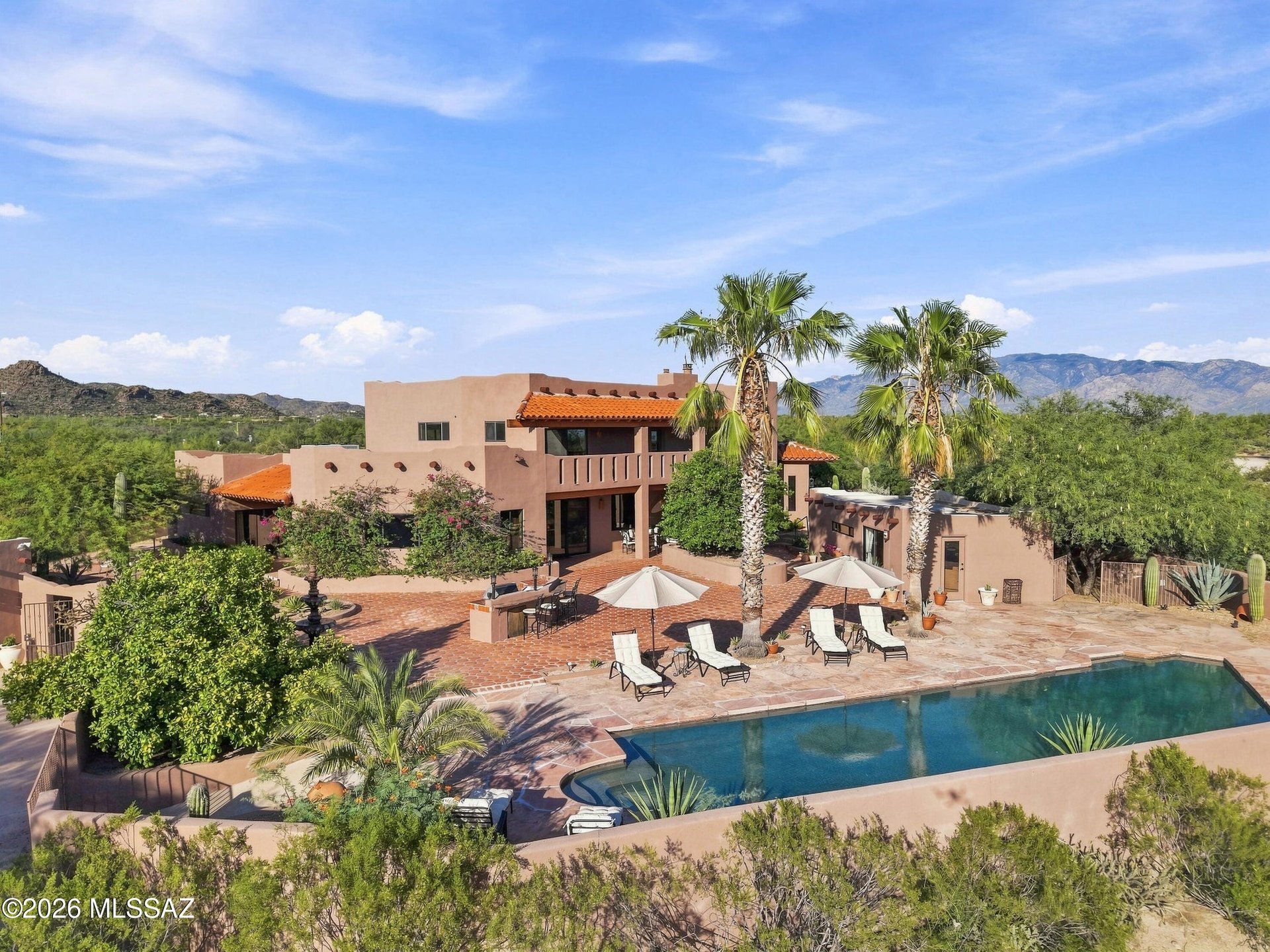 Southwestern-style home with a pool, palm trees, and mountains in the distance.