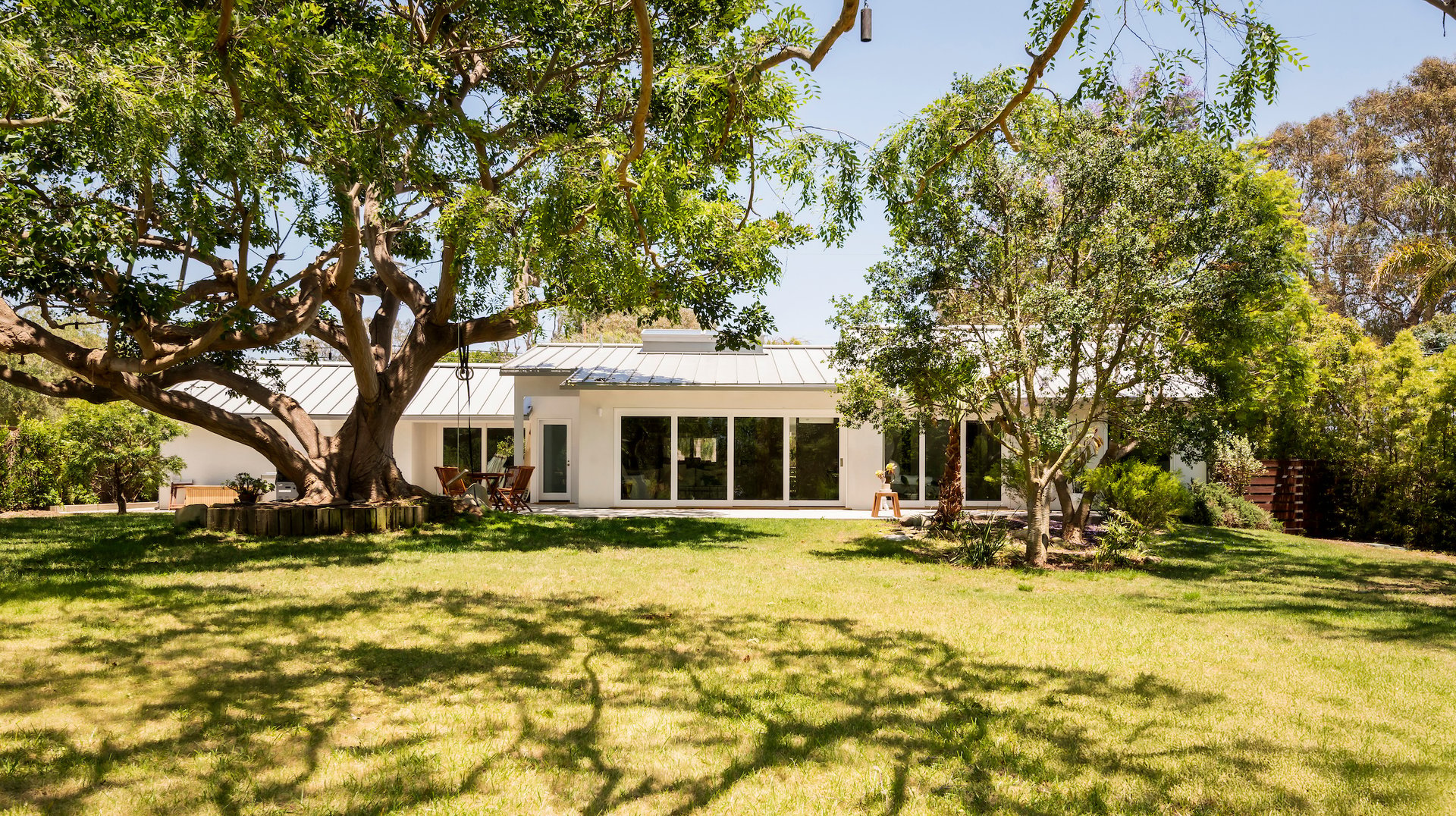 Modern white home behind a broad lawn, shaded by large mature trees.