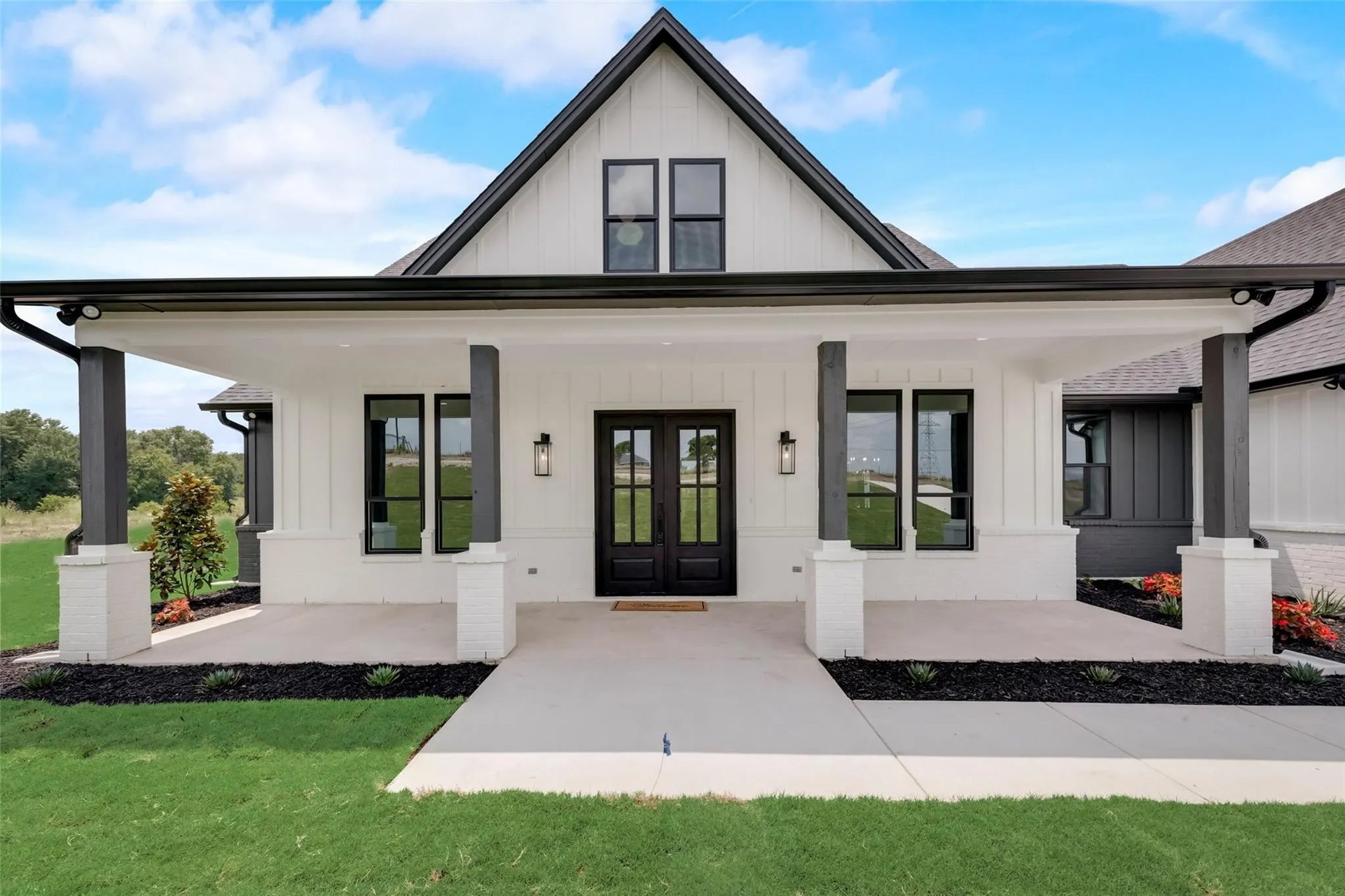White home with a steep front gable, covered porch, black trim, and landscaped lawn.