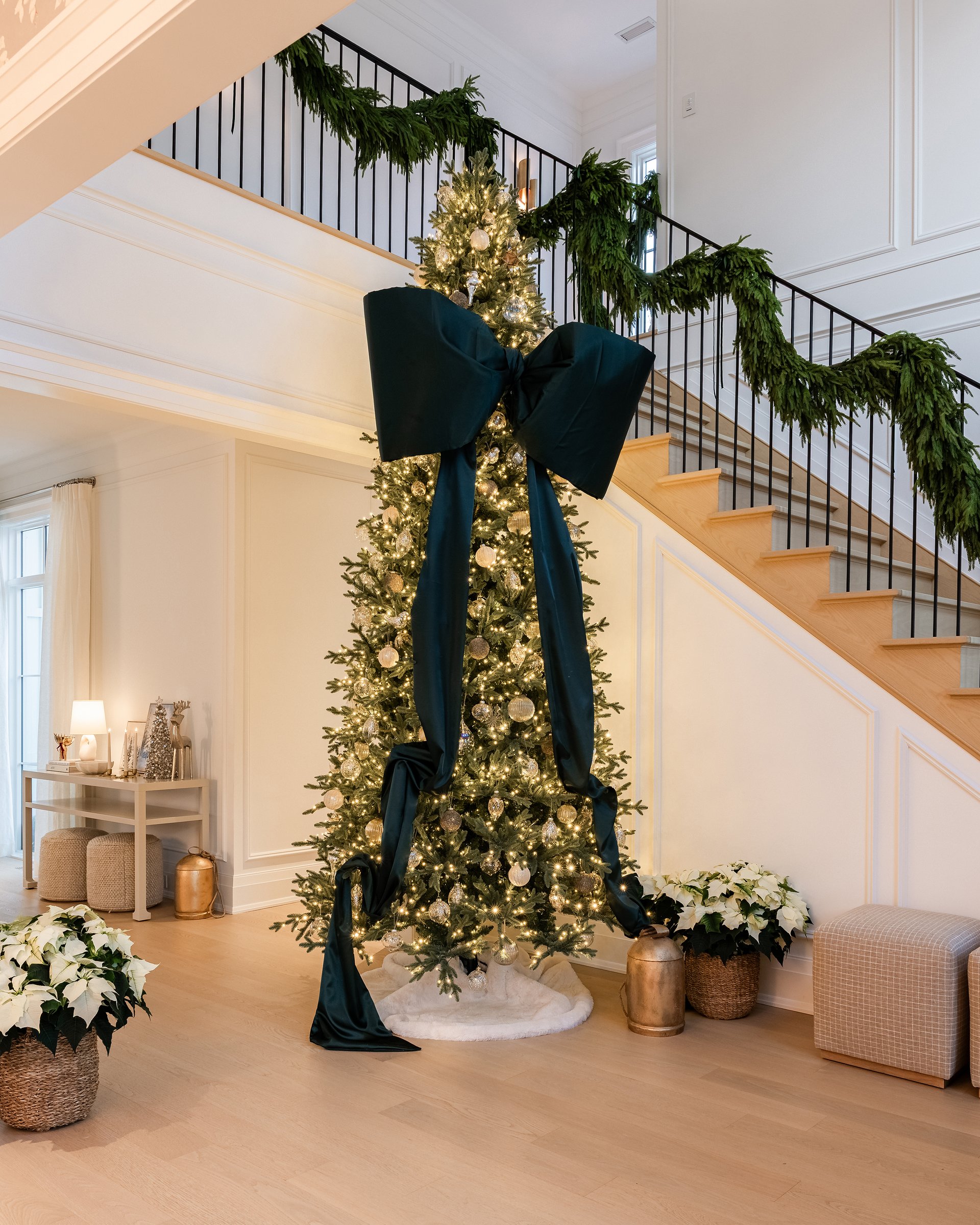 Holiday tree with oversized satin bow in an Oakville custom home, styled alongside staircase greenery garland.