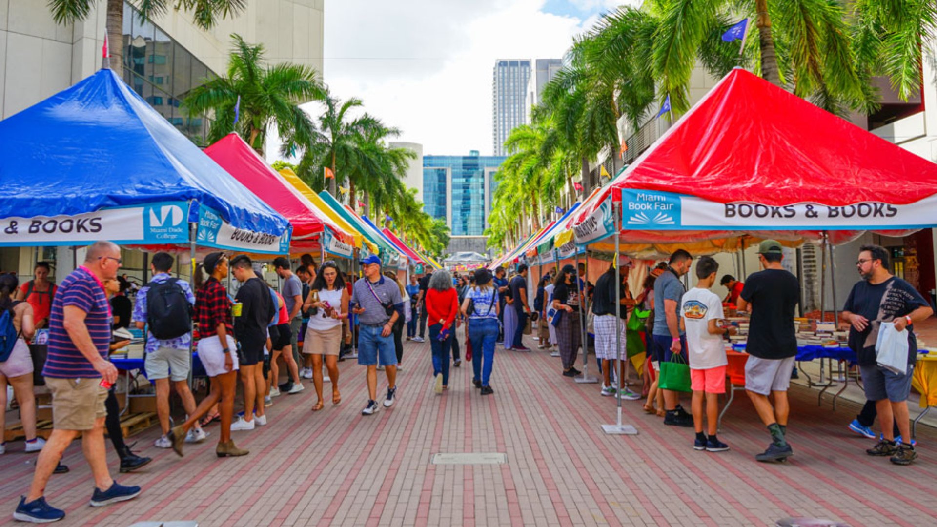 Miami Book Fair with blue and red vendor tents and crowds of people shopping for books along palm tree lined downtown street