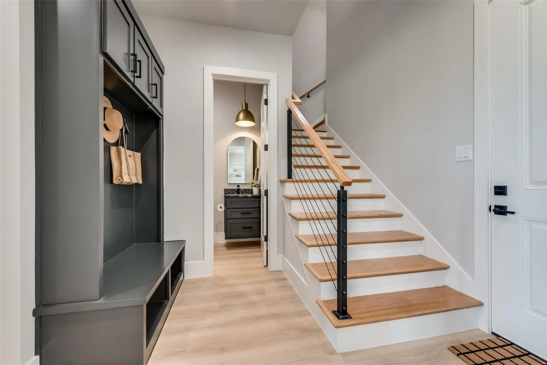 Entryway with built-in mudroom bench and cubbies beside a wood-tread staircase with black metal railing.