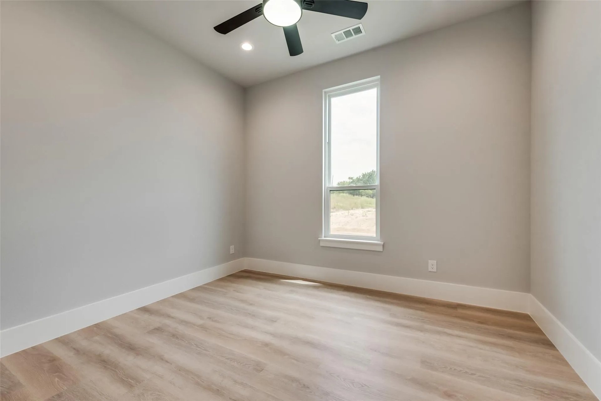 Empty bedroom with a ceiling fan, wood-look flooring, and a tall window.