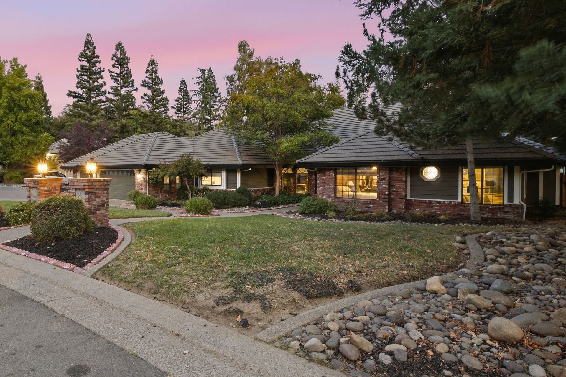 Single-story home with brick accents, a tiled roof, and a landscaped front yard at dusk.