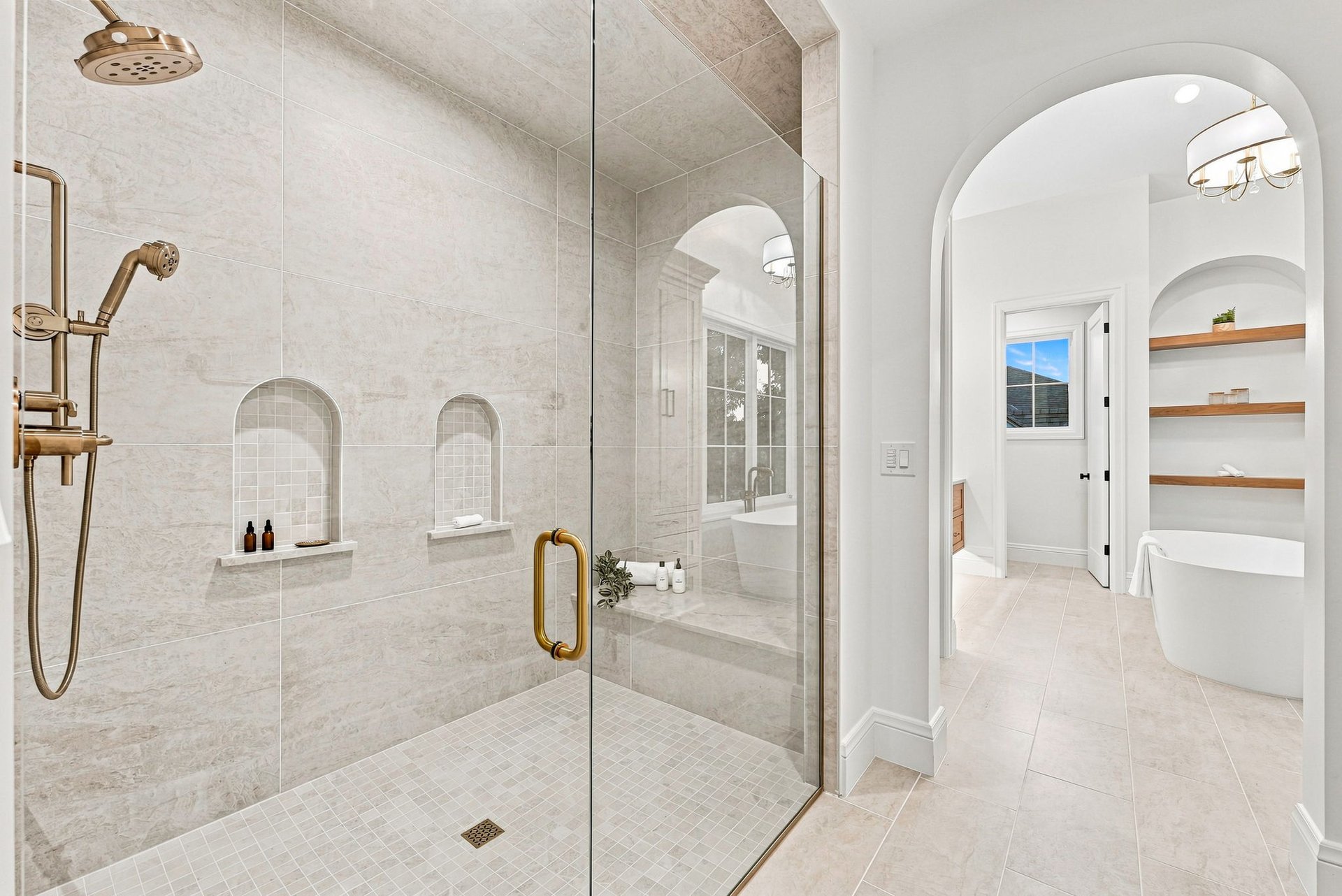 Bathroom with a glass-enclosed stone shower, brass fixtures, and an arched soaking tub alcove.