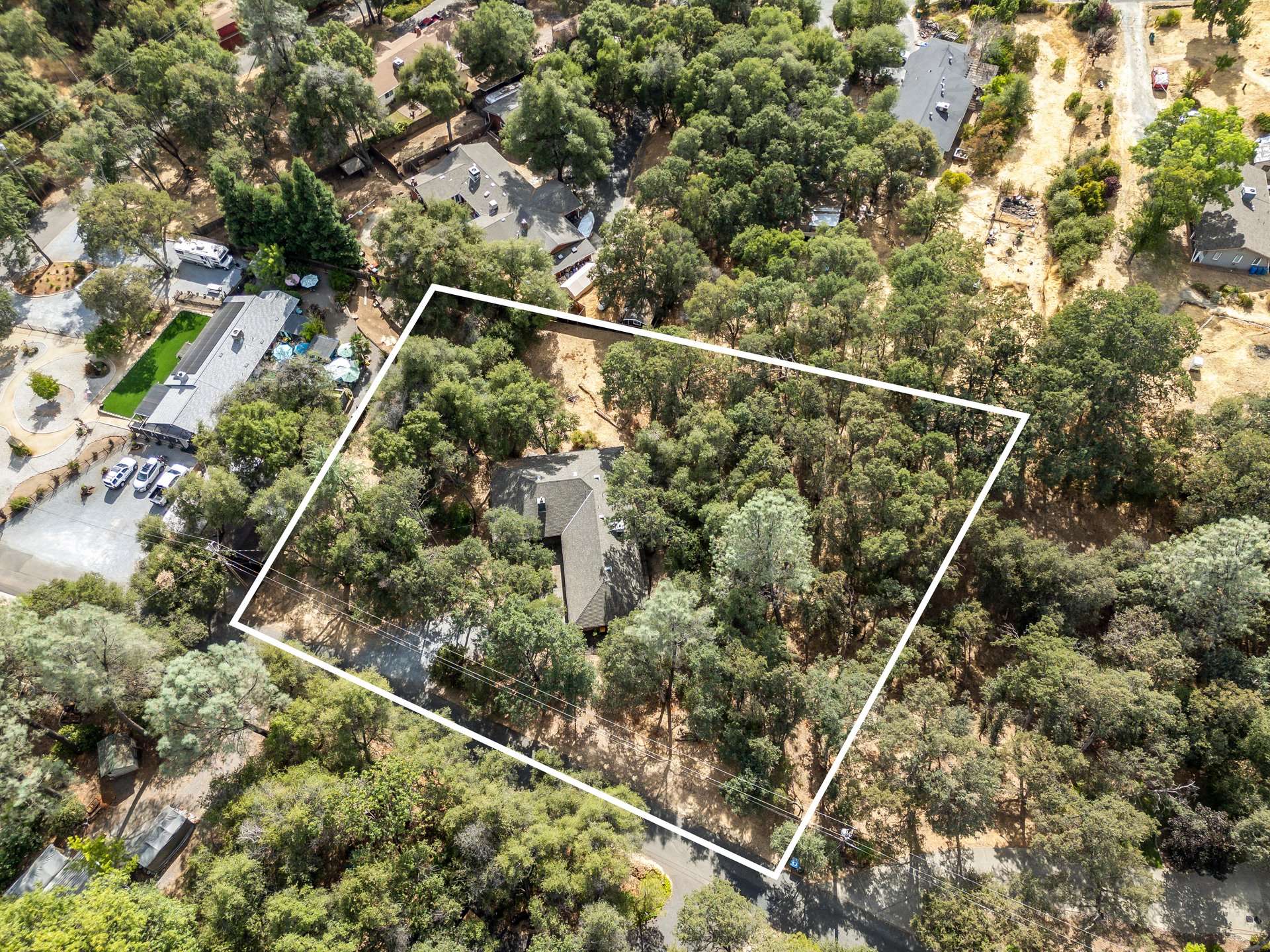 Aerial view of a wooded residential lot outlined in white, with a house near the center.