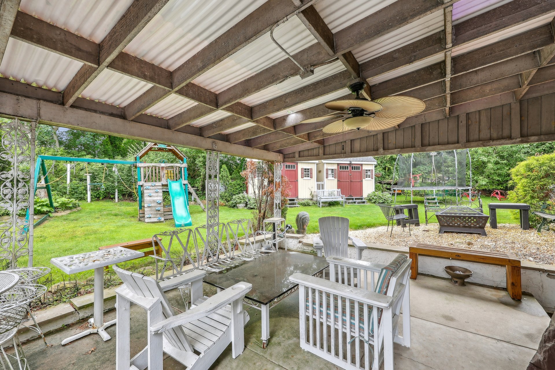 Covered patio with outdoor seating and ceiling fan overlooking a backyard playset and shed.