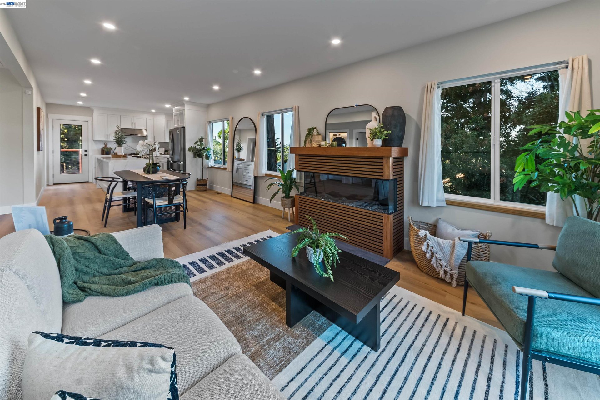 Open-plan living room with a slatted media console, striped rug, and adjoining kitchen and dining area.