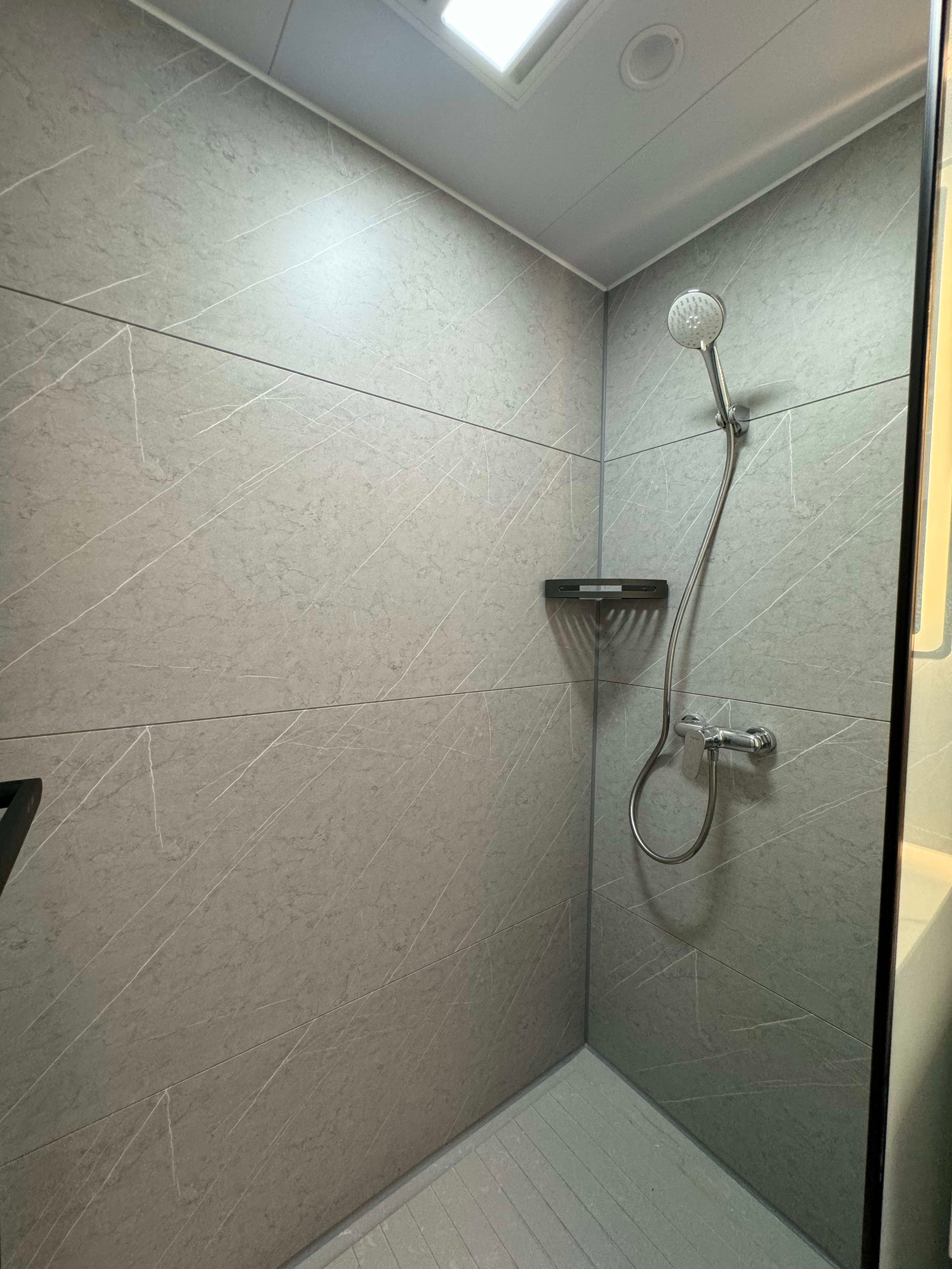 Walk-in shower with gray veined tile walls, handheld showerhead, and ceiling skylight.