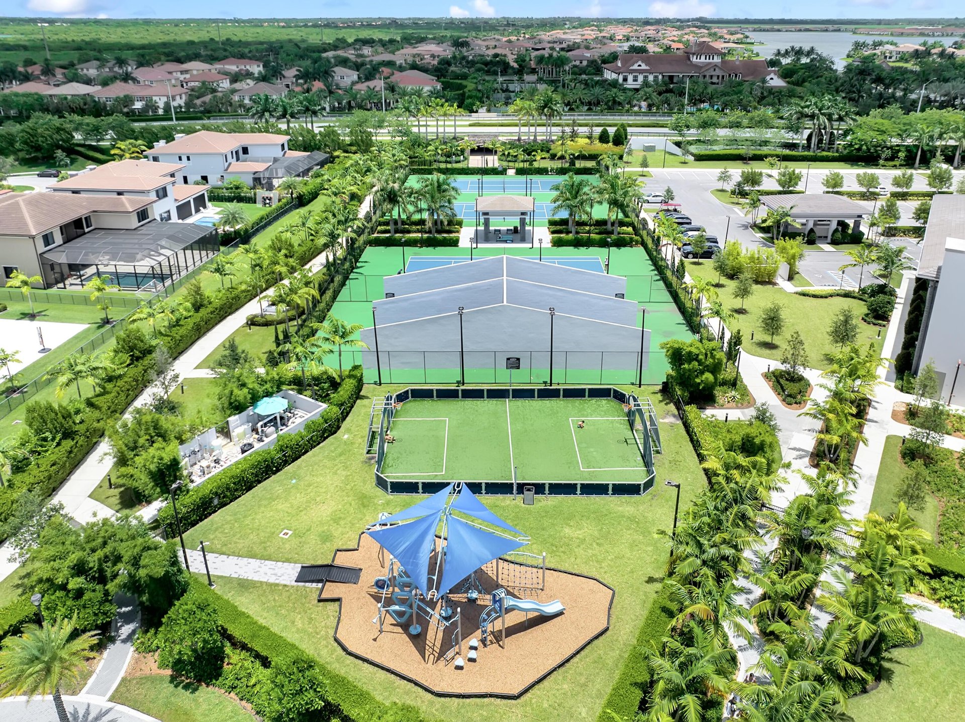 Community courts and a playground with blue shade canopies, surrounded by palm-lined homes.