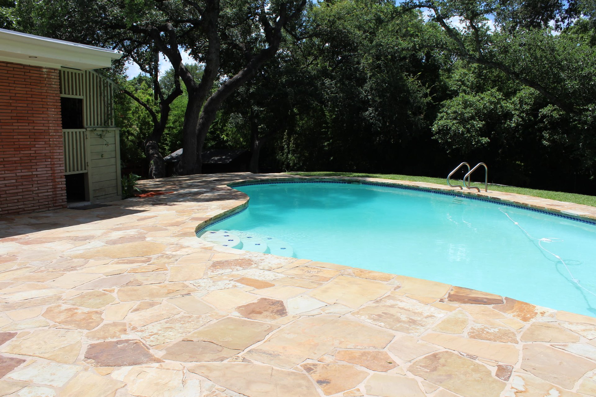 Outdoor pool with a flagstone patio, brick poolside structure, and mature trees.