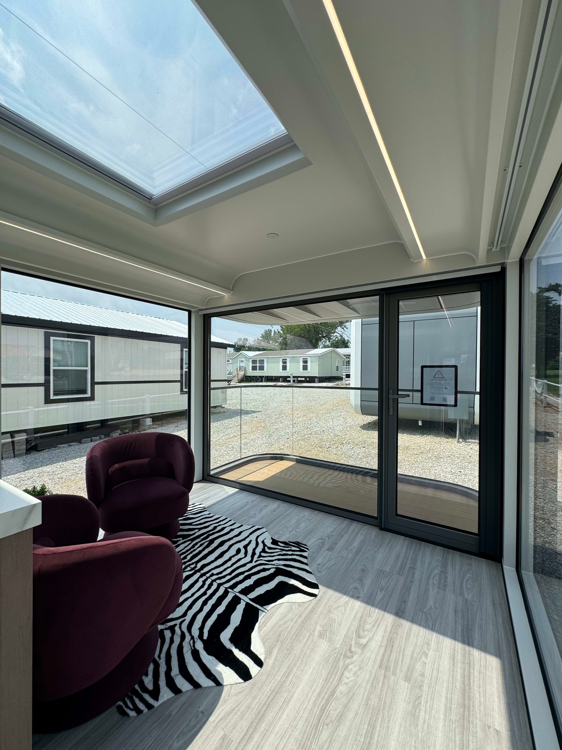 Tiny home living area with a large skylight, glass doors, burgundy chairs, and a zebra-print rug.