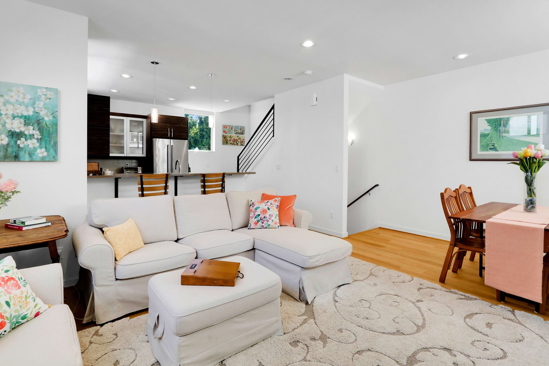 Open-plan living room with a white sectional, patterned rug, and dark-cabinet kitchen.